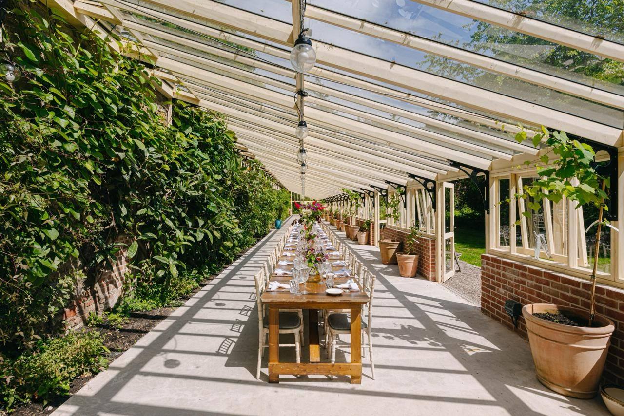 A long table set for lunch inside Birkhill's glass conservatory, walled garden beyond