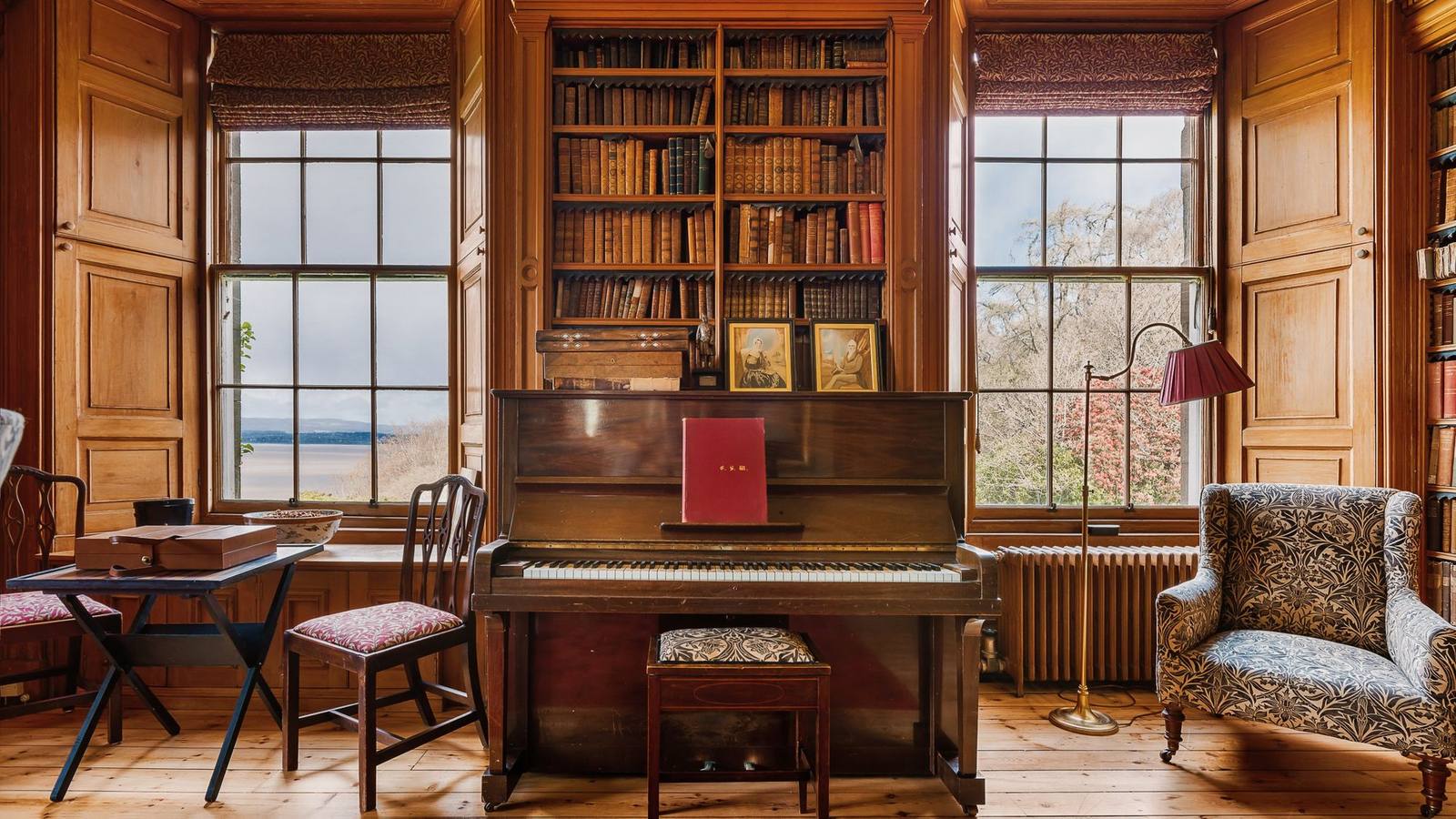 The library at Birkhill Castle, an upright piano beneath the bookshelves and a view over the Tay