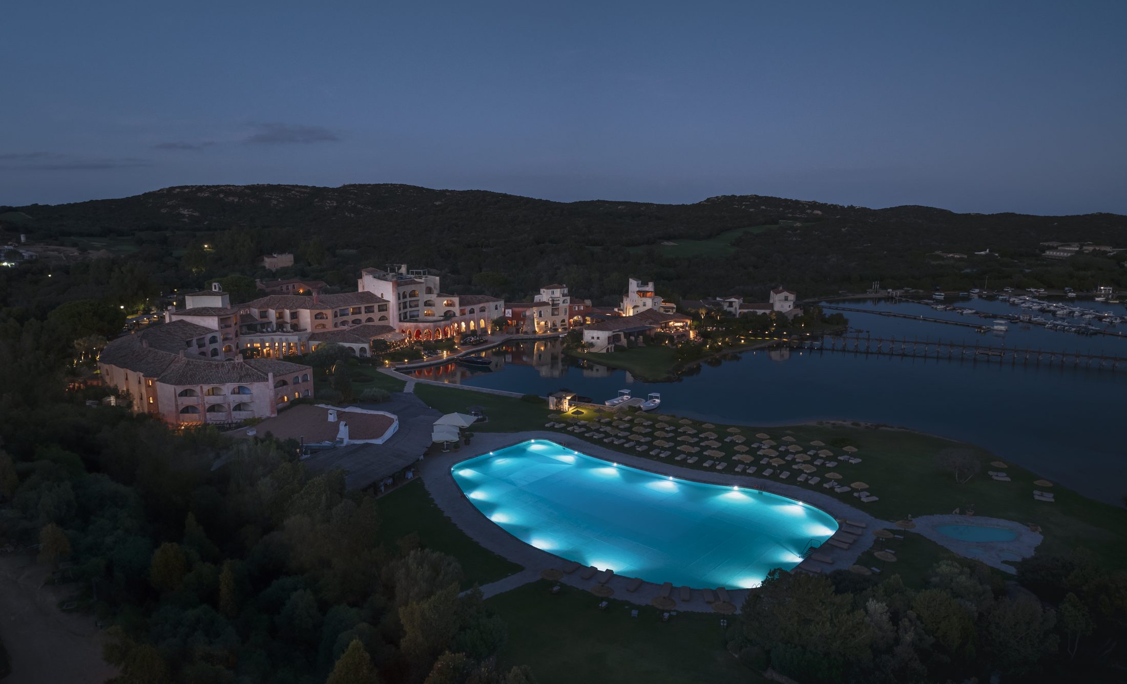 Hotel Cala di Volpe at night from above, its illuminated pool glowing beside the bay