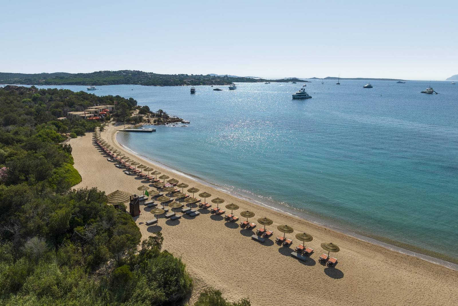 A curved white-sand beach with umbrellas along clear turquoise water on the Costa Smeralda