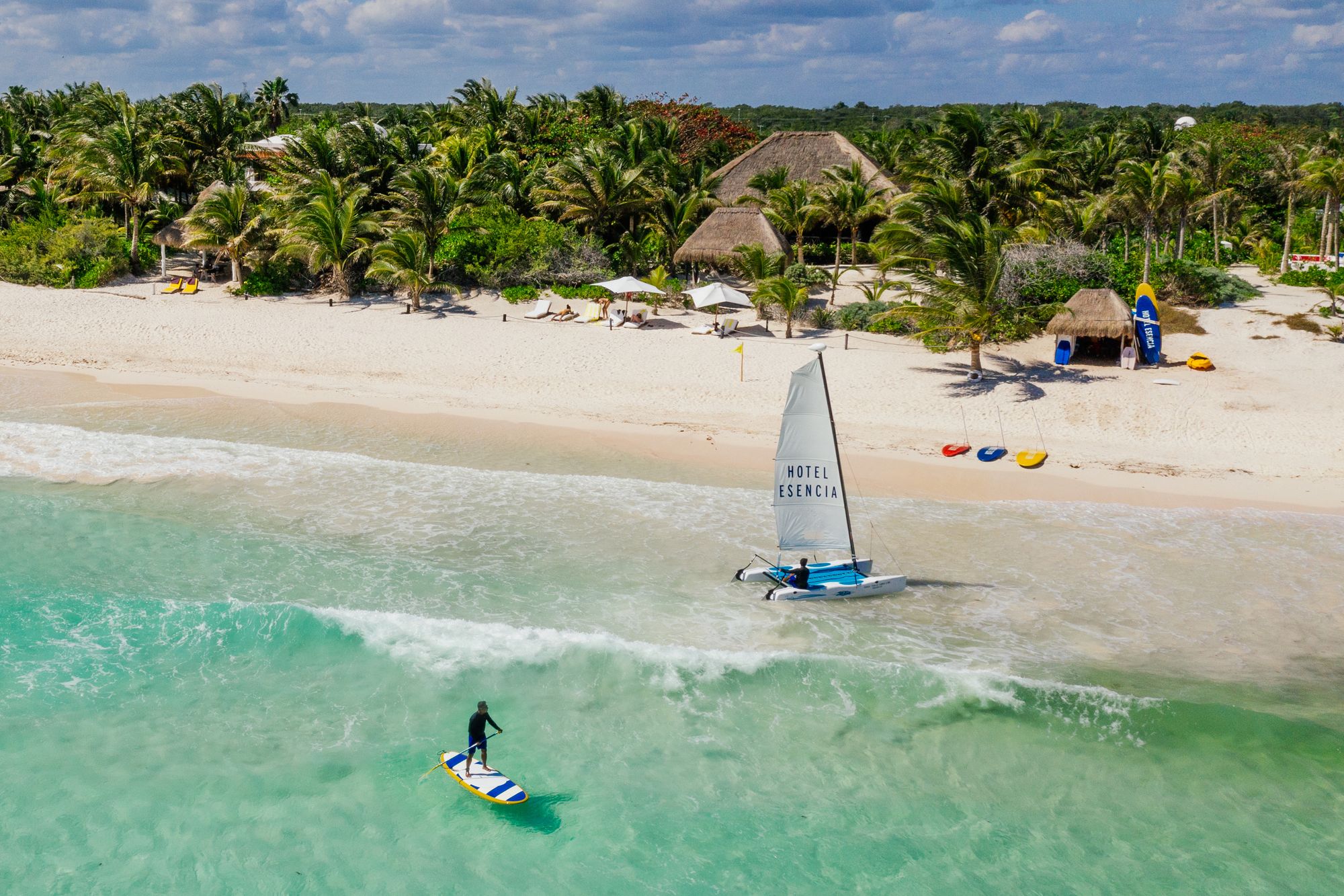 Paddleboarder and catamaran on the turquoise water off Hotel Esencia's beach