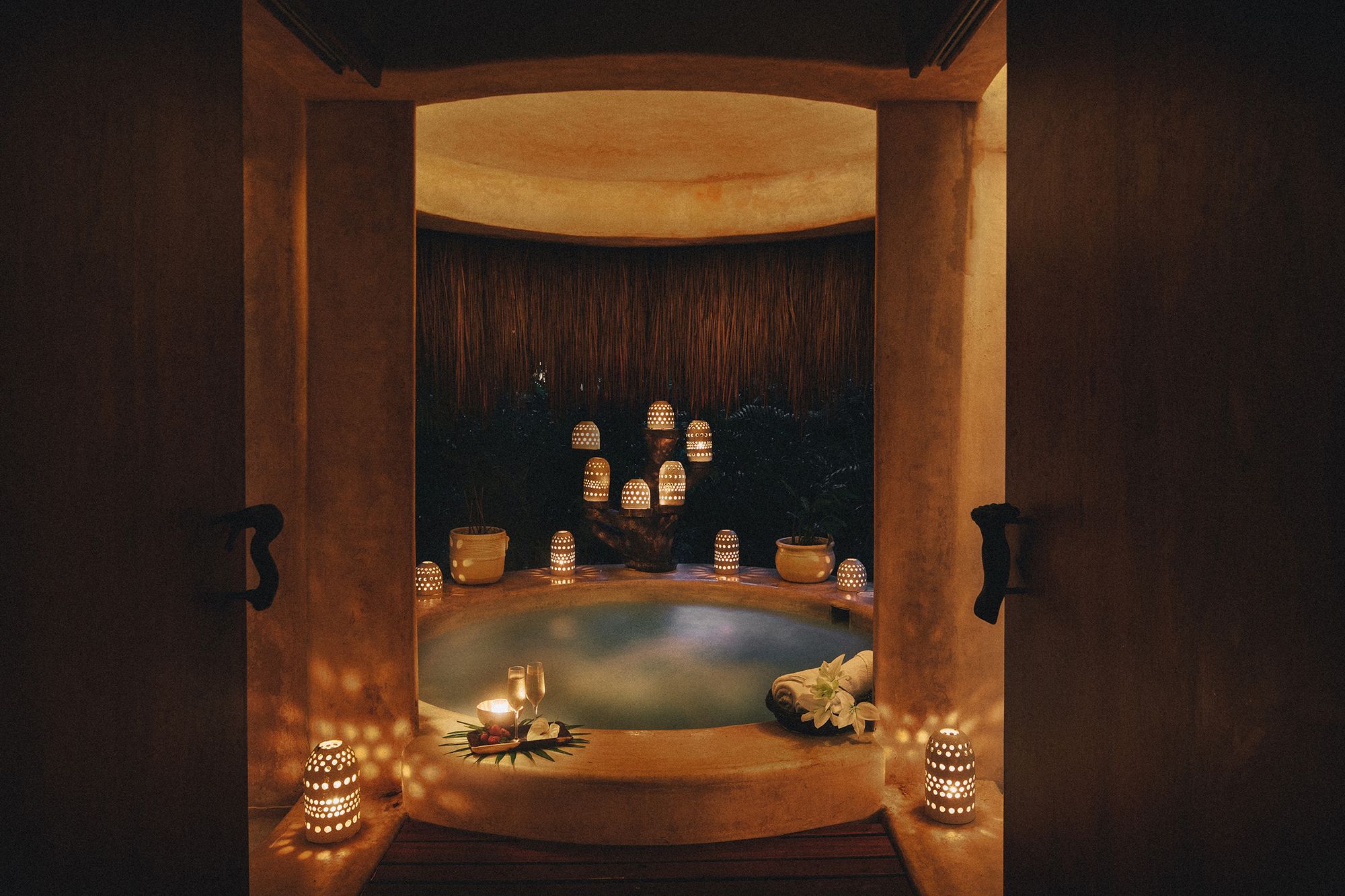 Candlelit circular hydrotherapy bath under a thatched roof at Esencia Spa