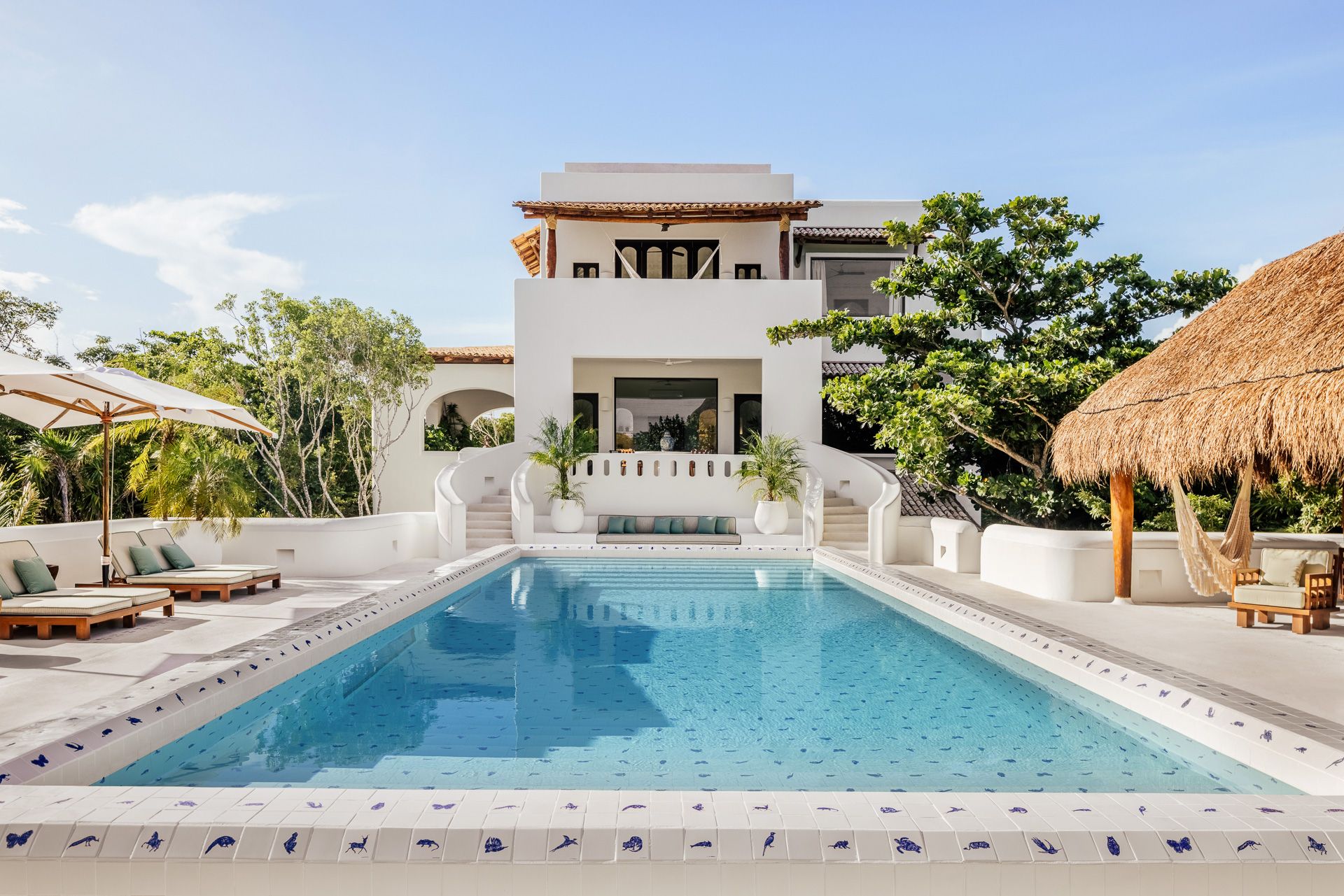 The Esencia Mansion and its pool, framed by palapa umbrellas, at Hotel Esencia