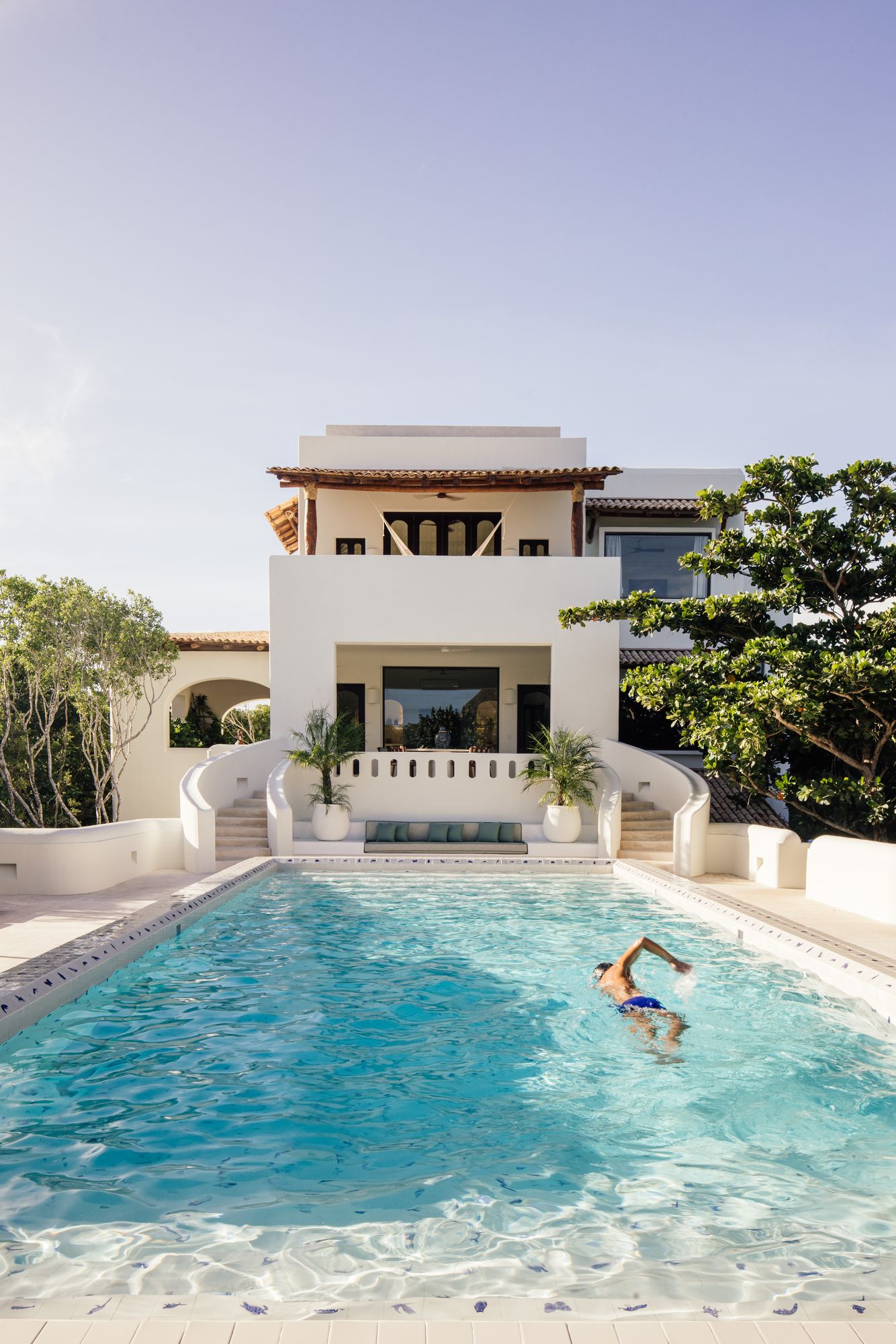 Swimmer in the Esencia Mansion's pool beneath the white villa