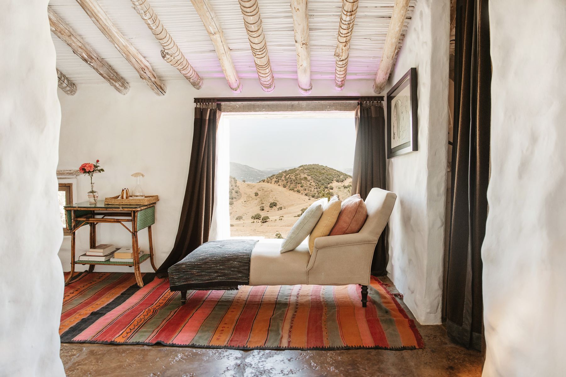 A white suite with a striped rug and a window opening onto mountains