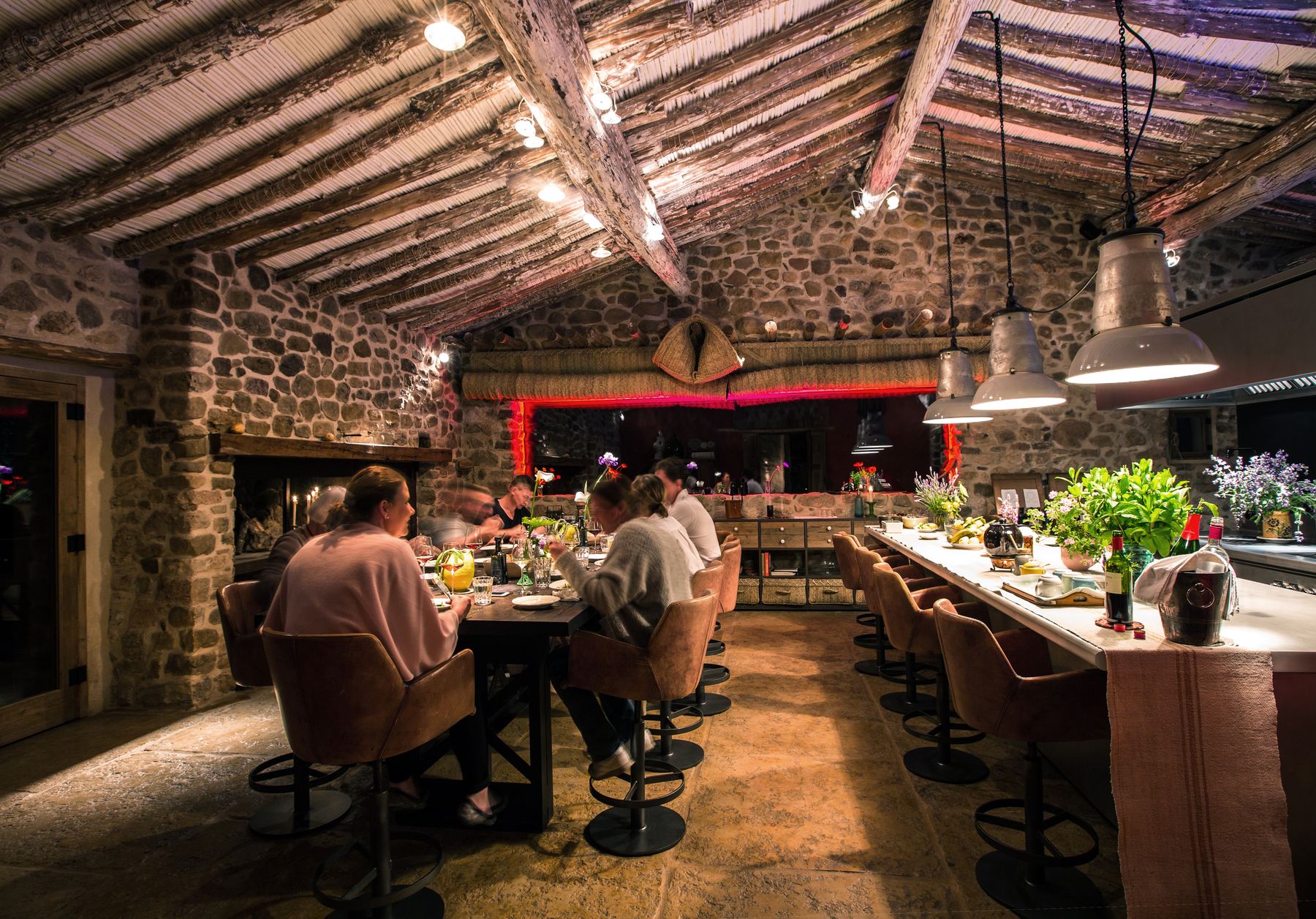 The candlelit dining room under a timber ceiling, guests seated at a long counter beside the open kitchen