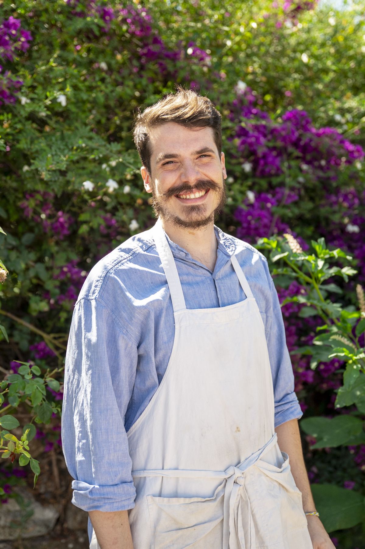 Chef Manuel Vargas smiling in an apron in front of bougainvillea
