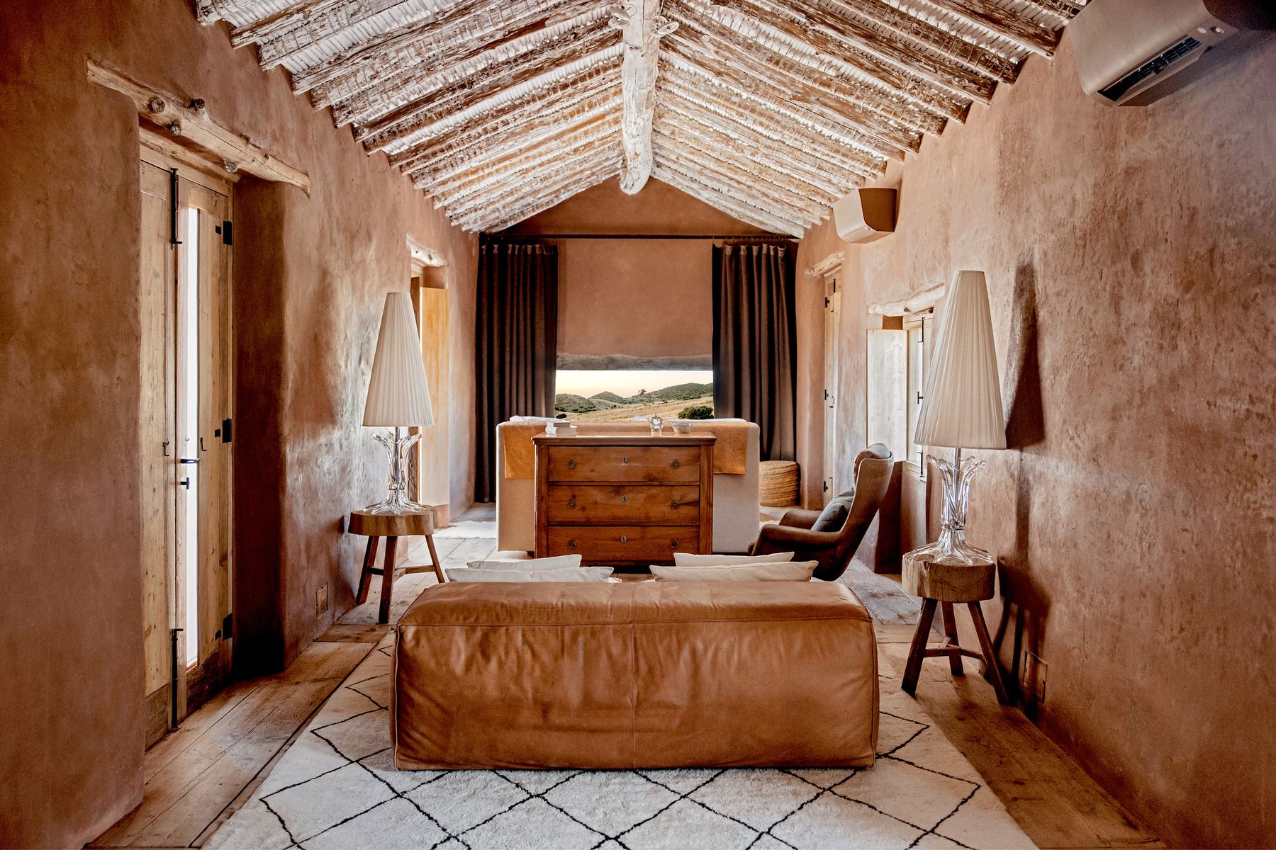 A long suite with timber and cane ceiling, Berber rug and leather armchairs