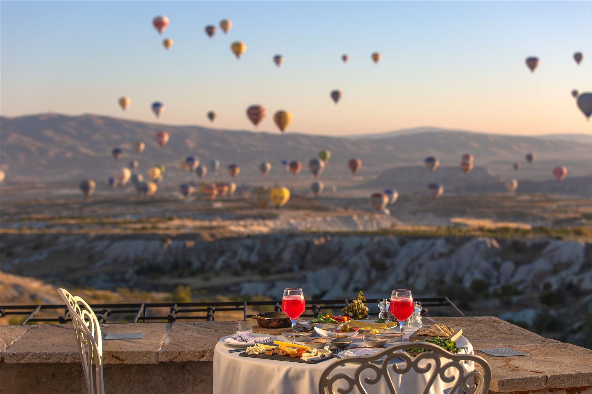 Breakfast table on a terrace overlooking the Cappadocia valleys as dozens of hot air balloons rise at sunrise