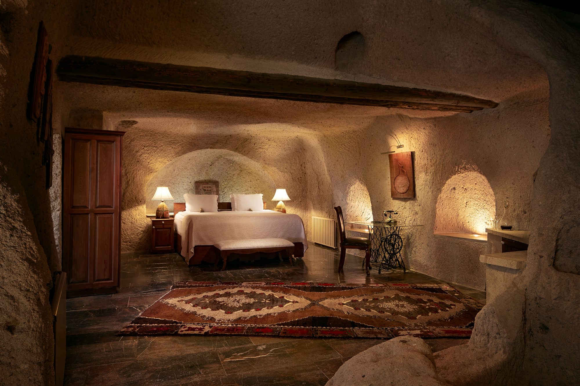 Candlelit cave suite at Museum Hotel, Cappadocia, with a bed set beneath a carved stone ceiling and Turkish rugs