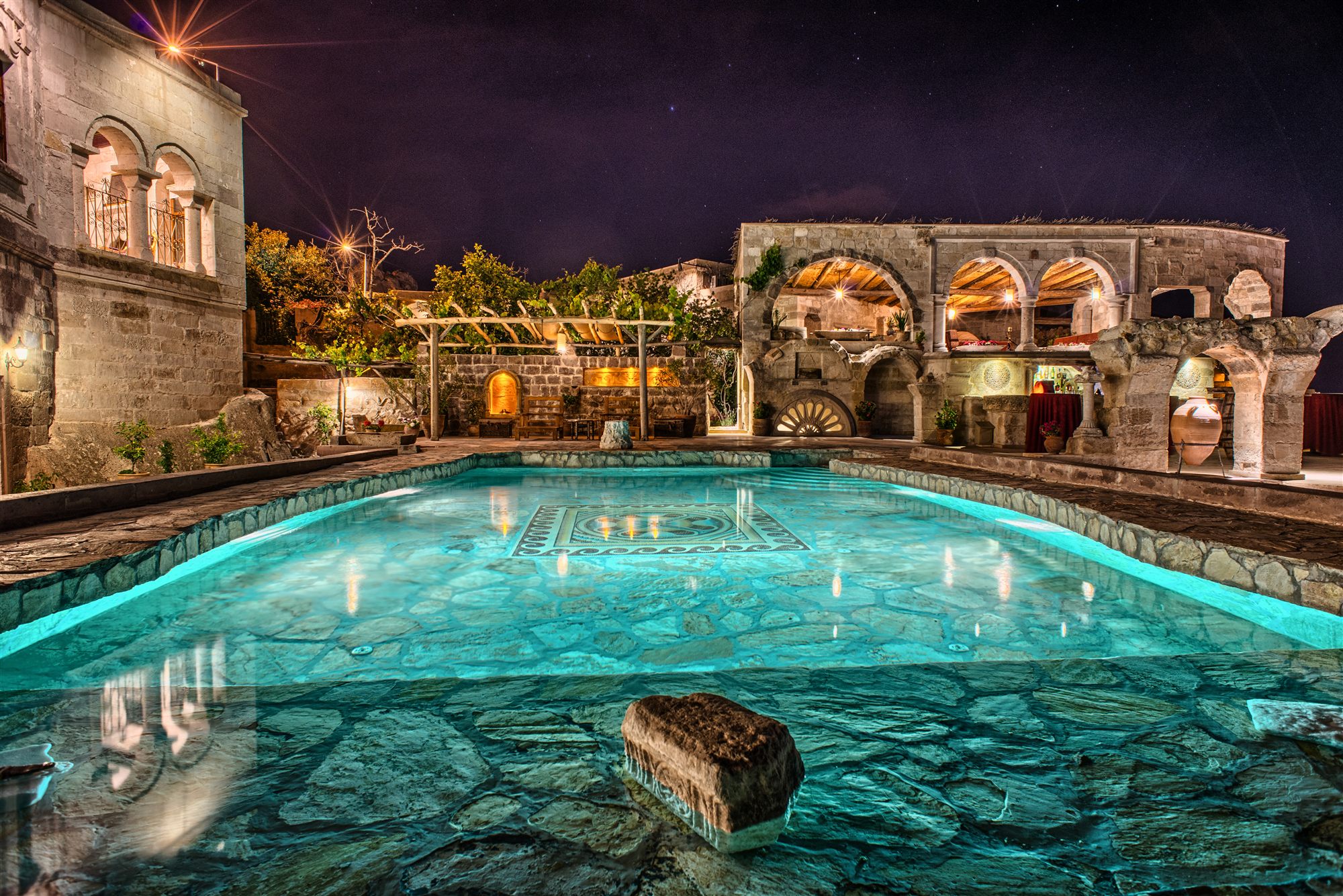 Outdoor pool at Museum Hotel, Cappadocia, glowing turquoise at night beneath illuminated stone buildings