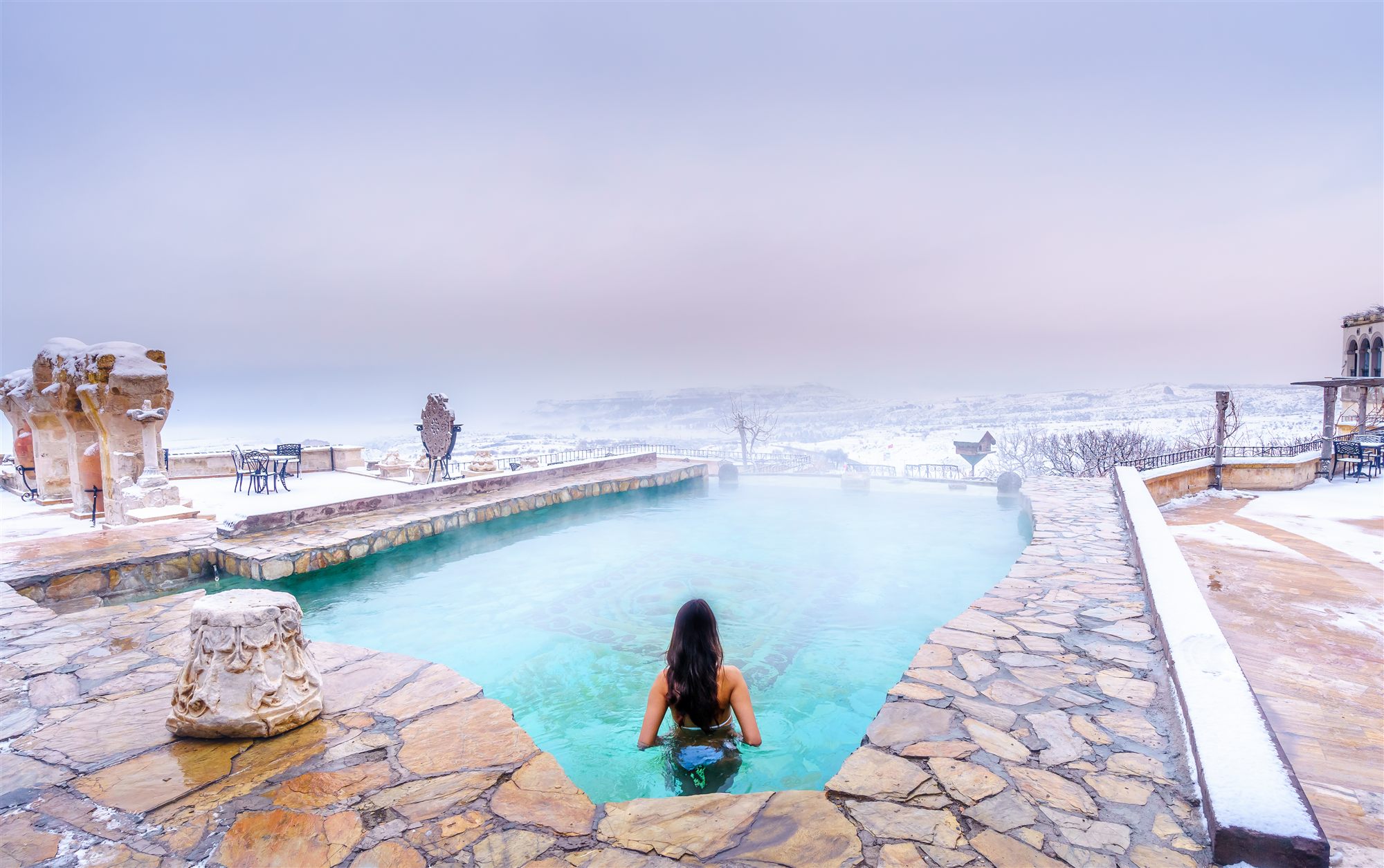 Guest in the steaming heated pool surrounded by snow in winter at Museum Hotel, Cappadocia