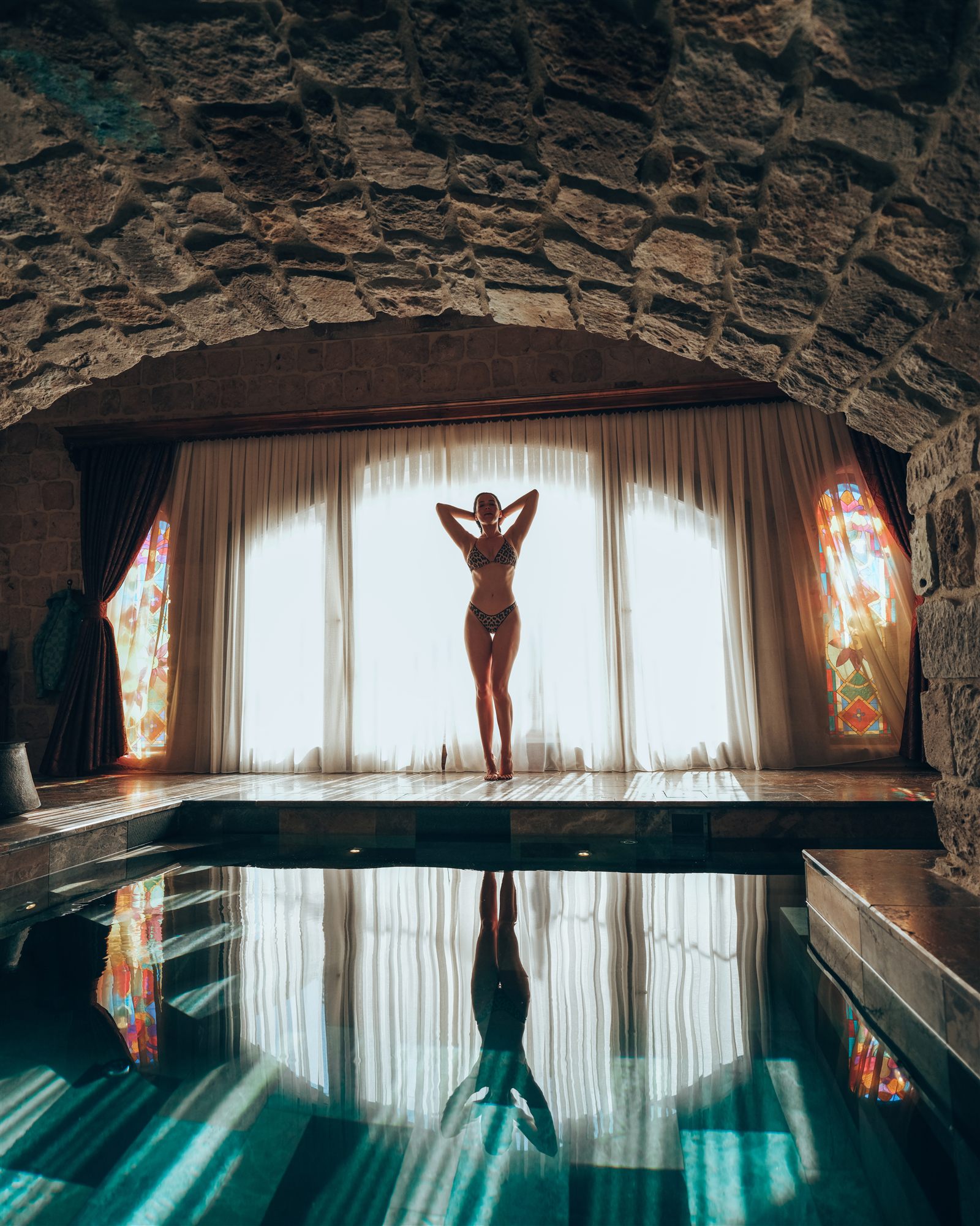 Woman silhouetted at a curtained window above a private indoor pool in a stone suite at Museum Hotel