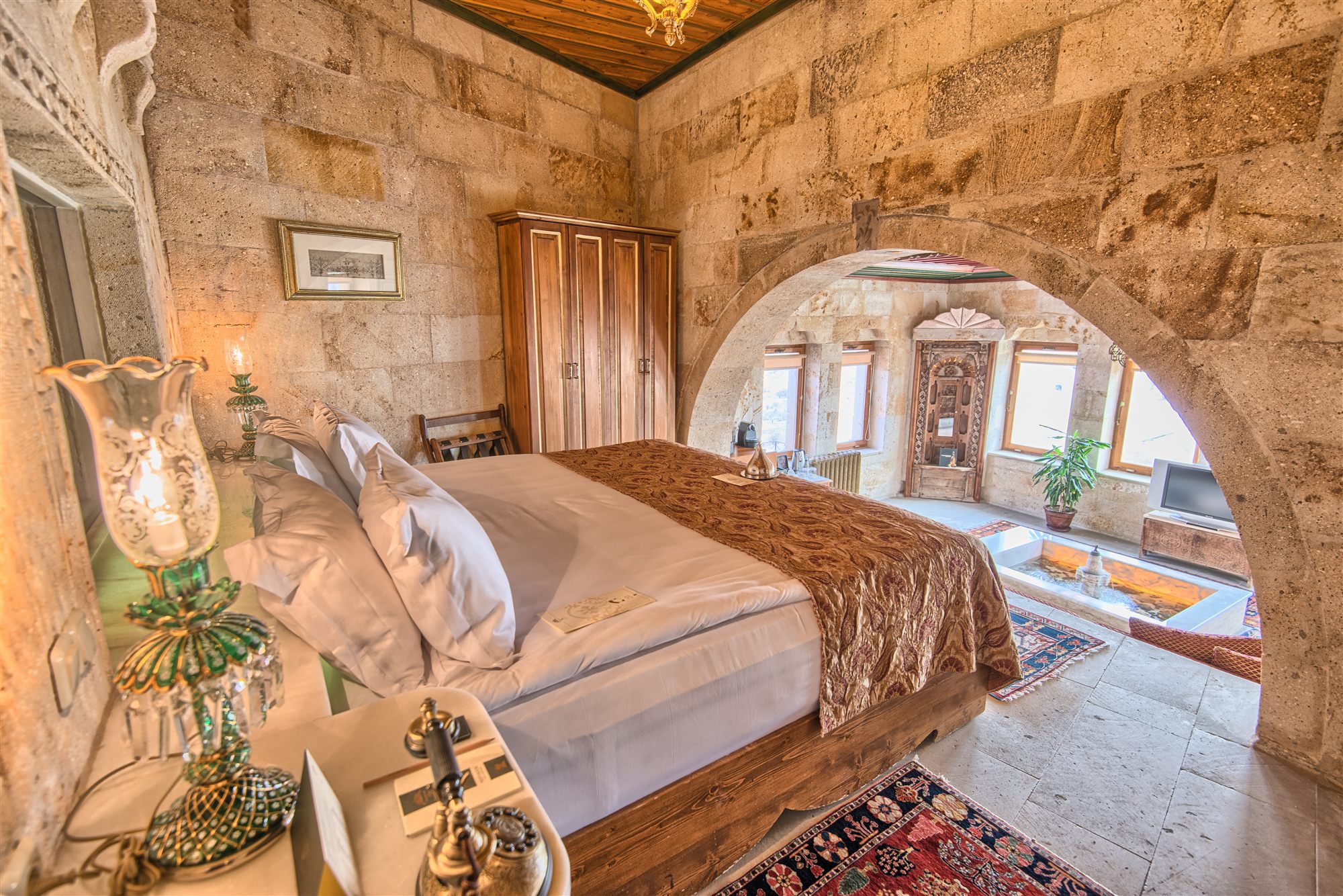 Stone house suite with antique furniture and an arched doorway at Museum Hotel, Cappadocia