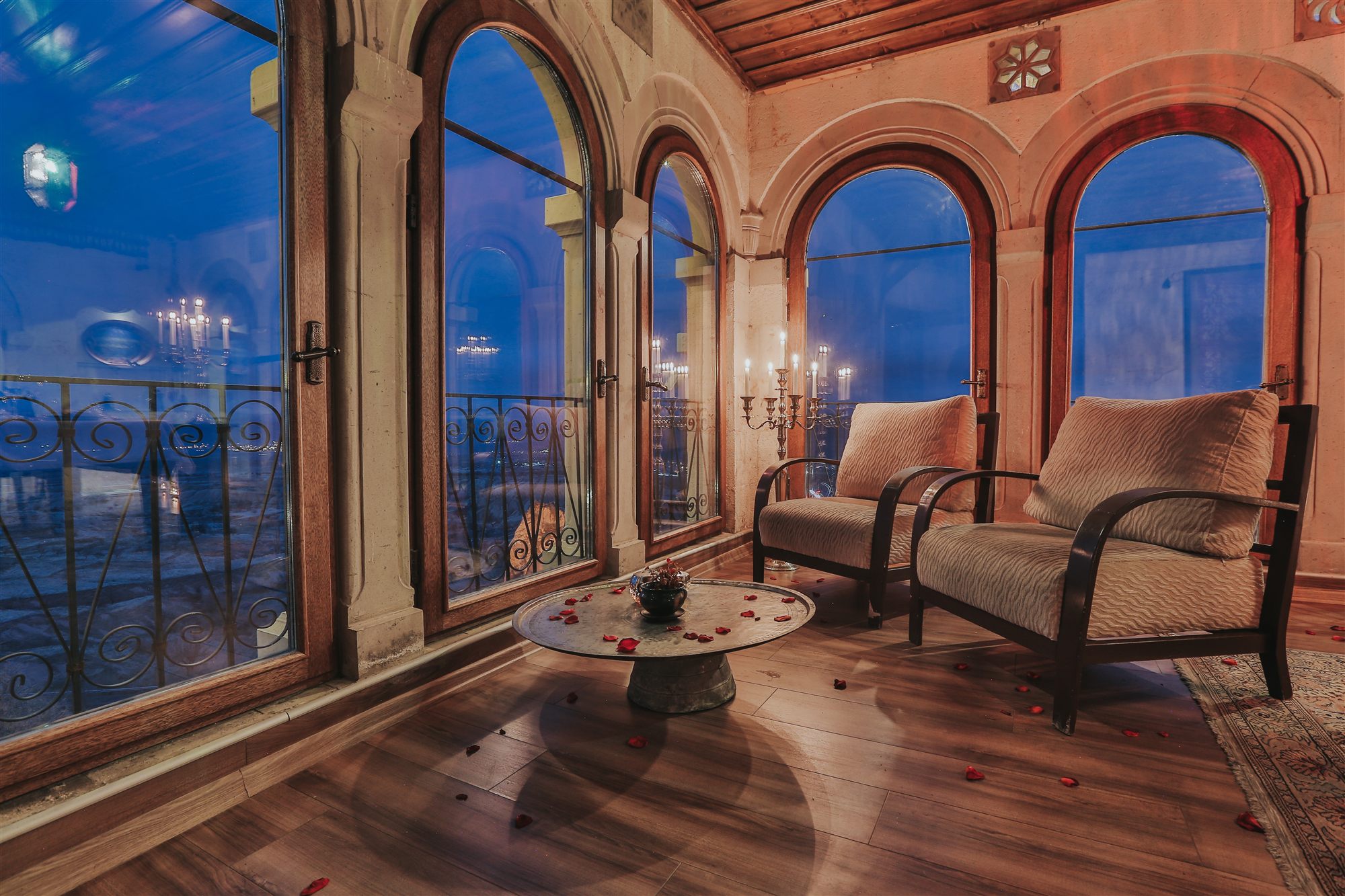 Suite lounge with armchairs and arched windows overlooking Cappadocia at dusk, Museum Hotel