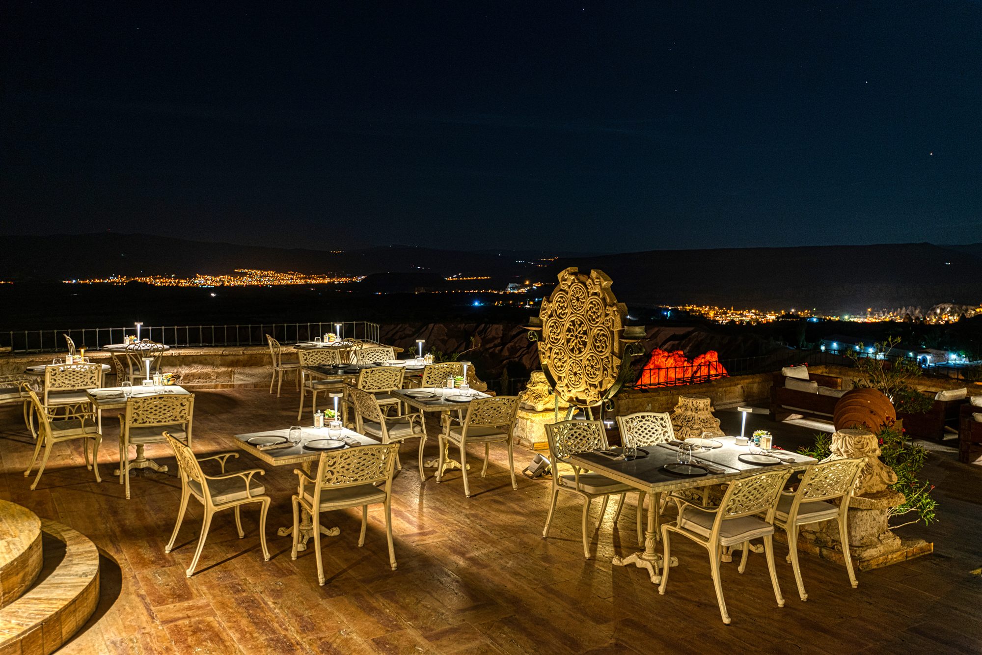 Terrace tables set for dinner at night at Museum Hotel with the lights of the Cappadocia villages below