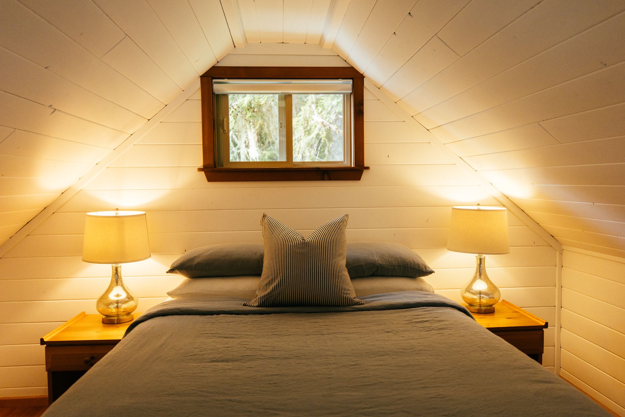 Lamp-lit bedroom under a sloping wooden ceiling in a forest cabin at Nimmo Bay