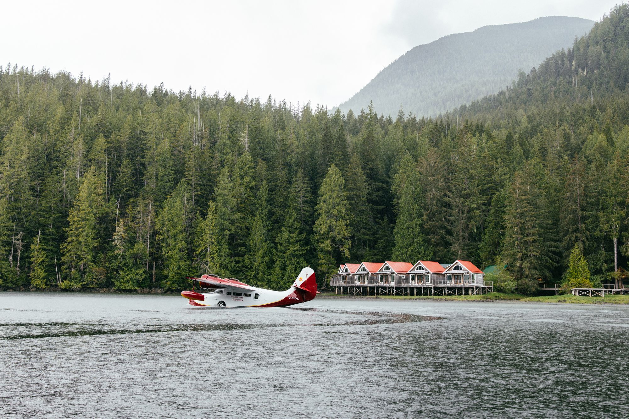 Floatplane landing in front of the red-roofed waterfront cabins of Nimmo Bay