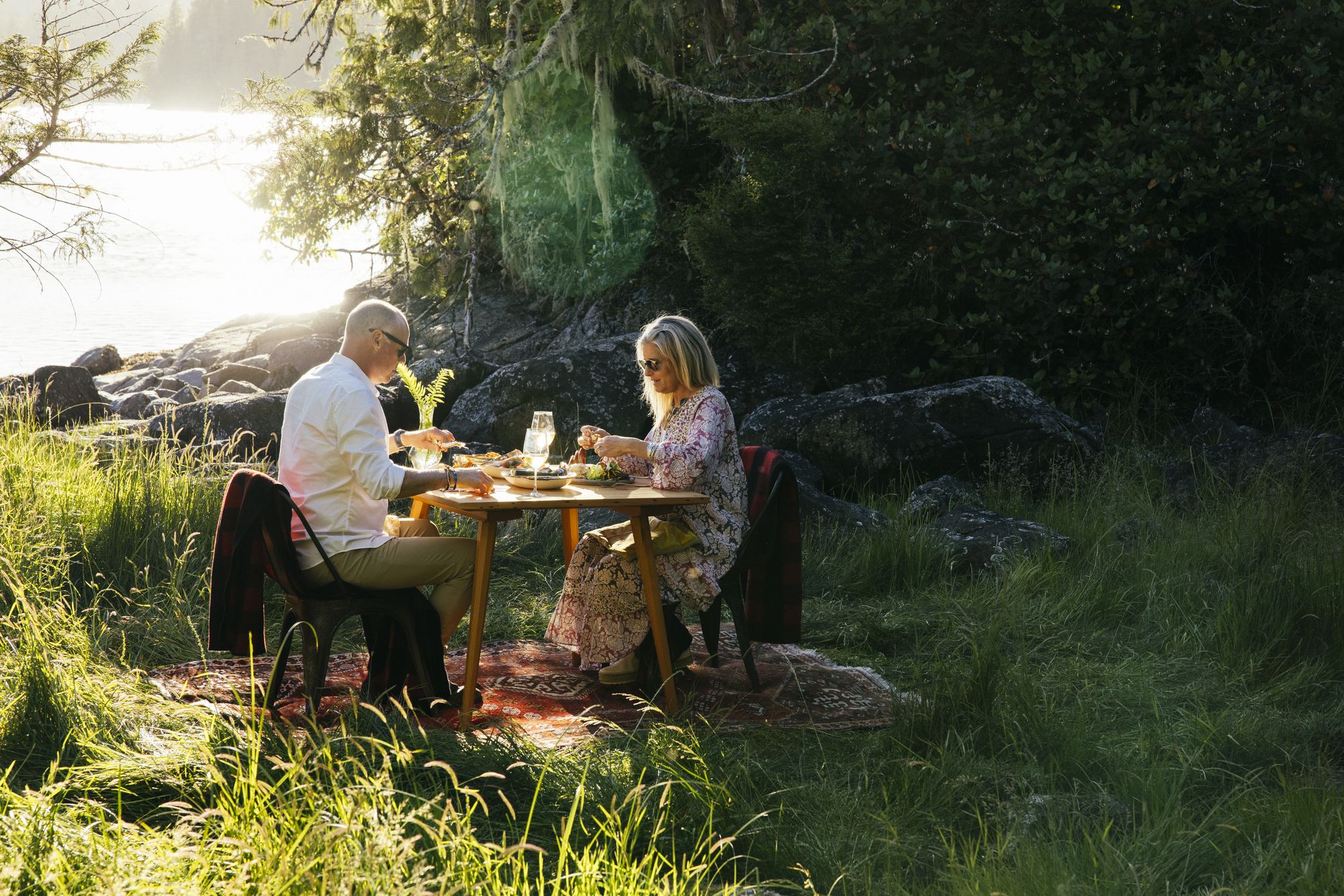 Couple sharing an outdoor lunch in a sunlit forest clearing at Nimmo Bay