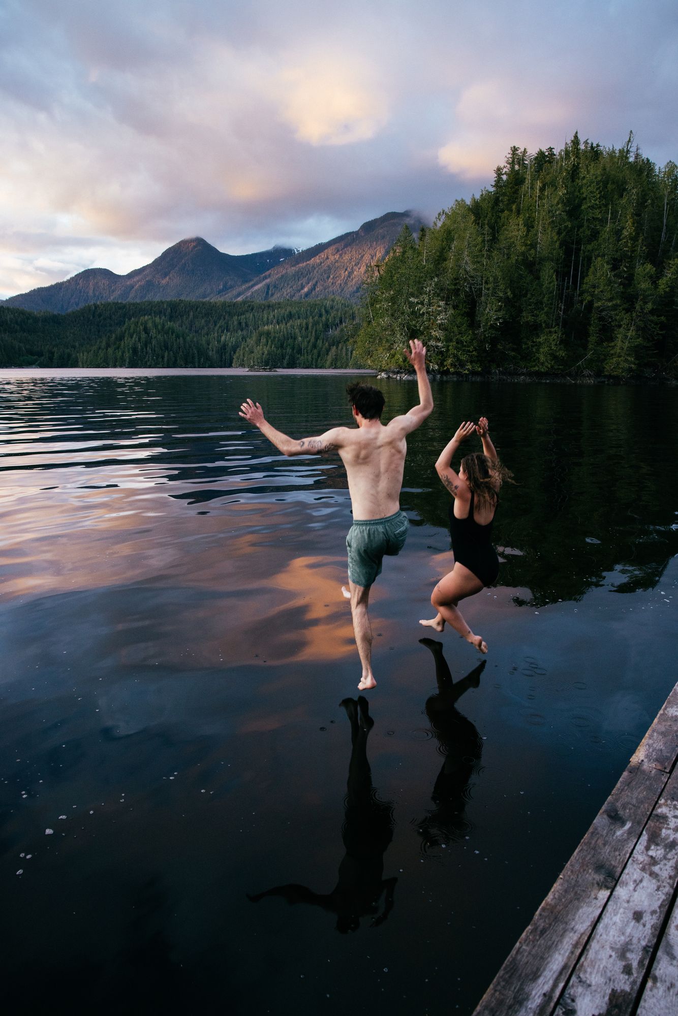 Two guests jumping from the sauna dock into the water at sunset, Nimmo Bay