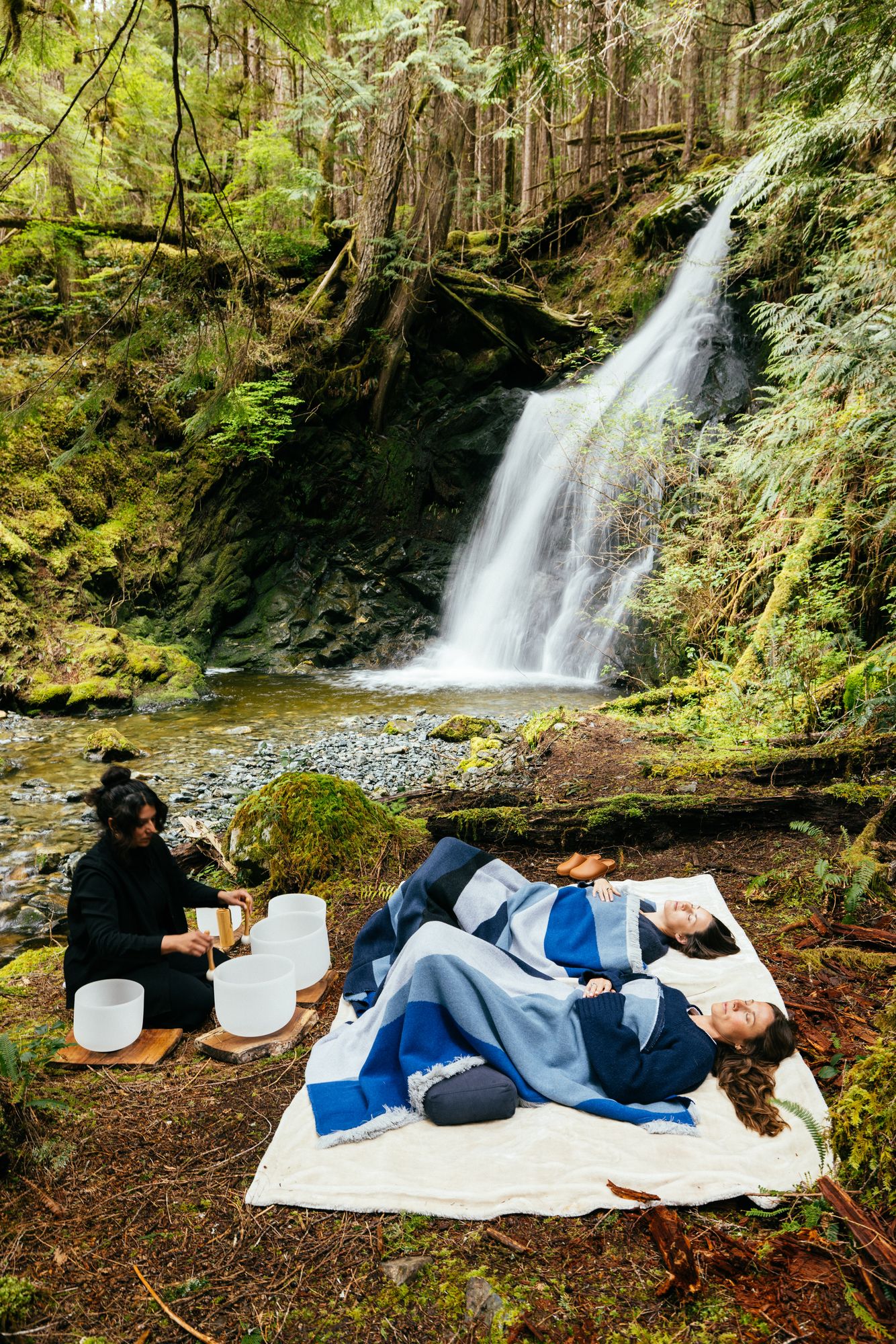 Sound bowl meditation on blankets beside a rainforest waterfall at Nimmo Bay
