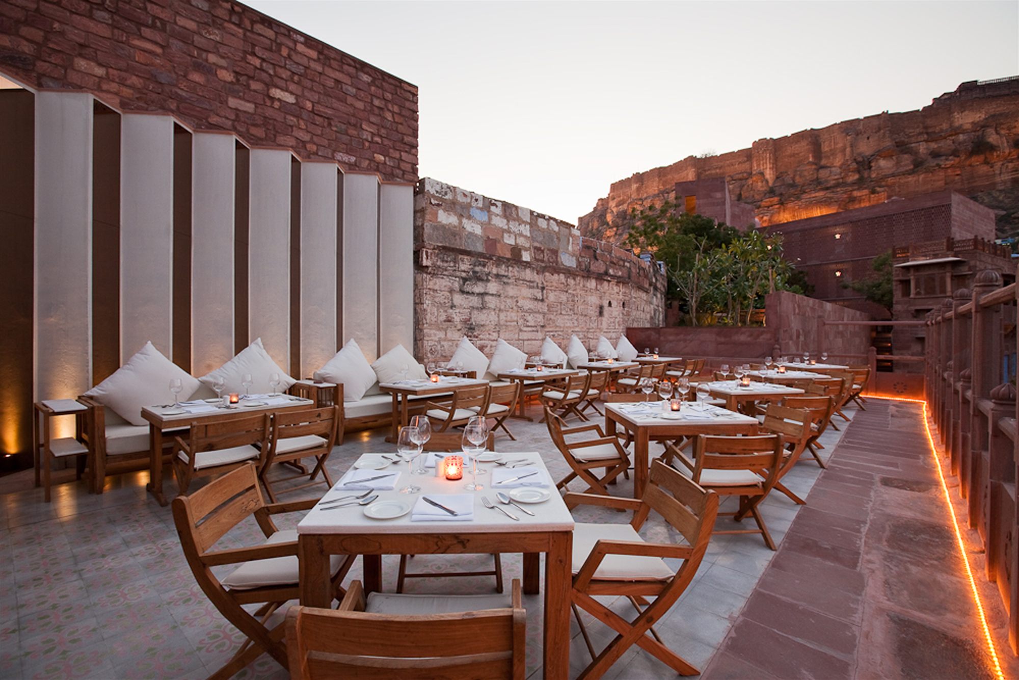 Darikhana open-air restaurant at RAAS Jodhpur with set tables and cushions facing Mehrangarh Fort