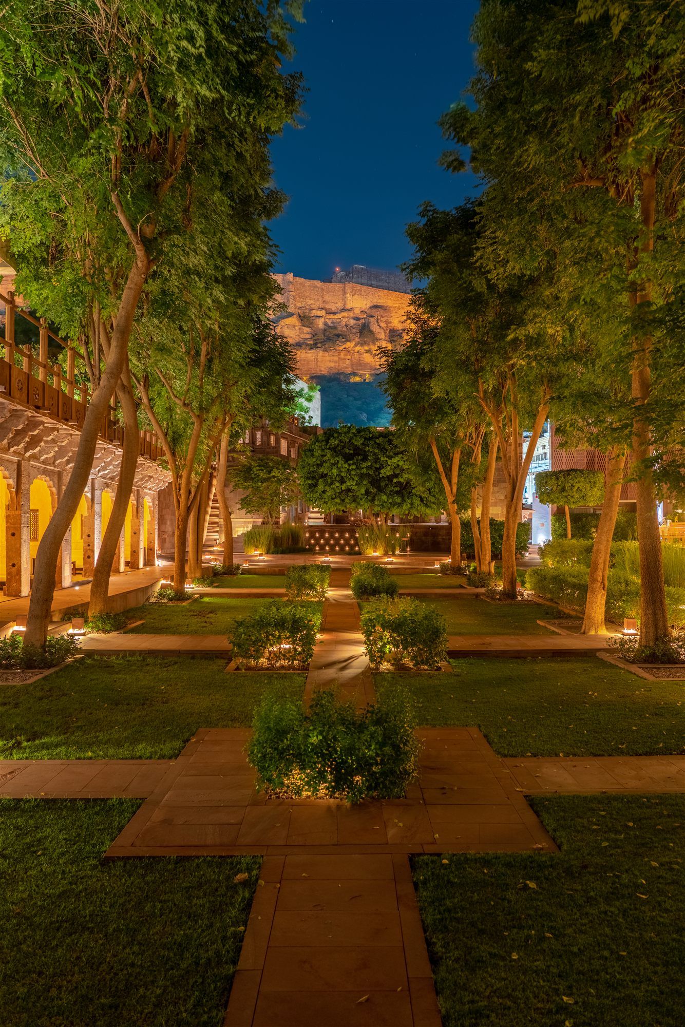 Lantern-lit garden path at night at RAAS Jodhpur with trees and Mehrangarh Fort beyond