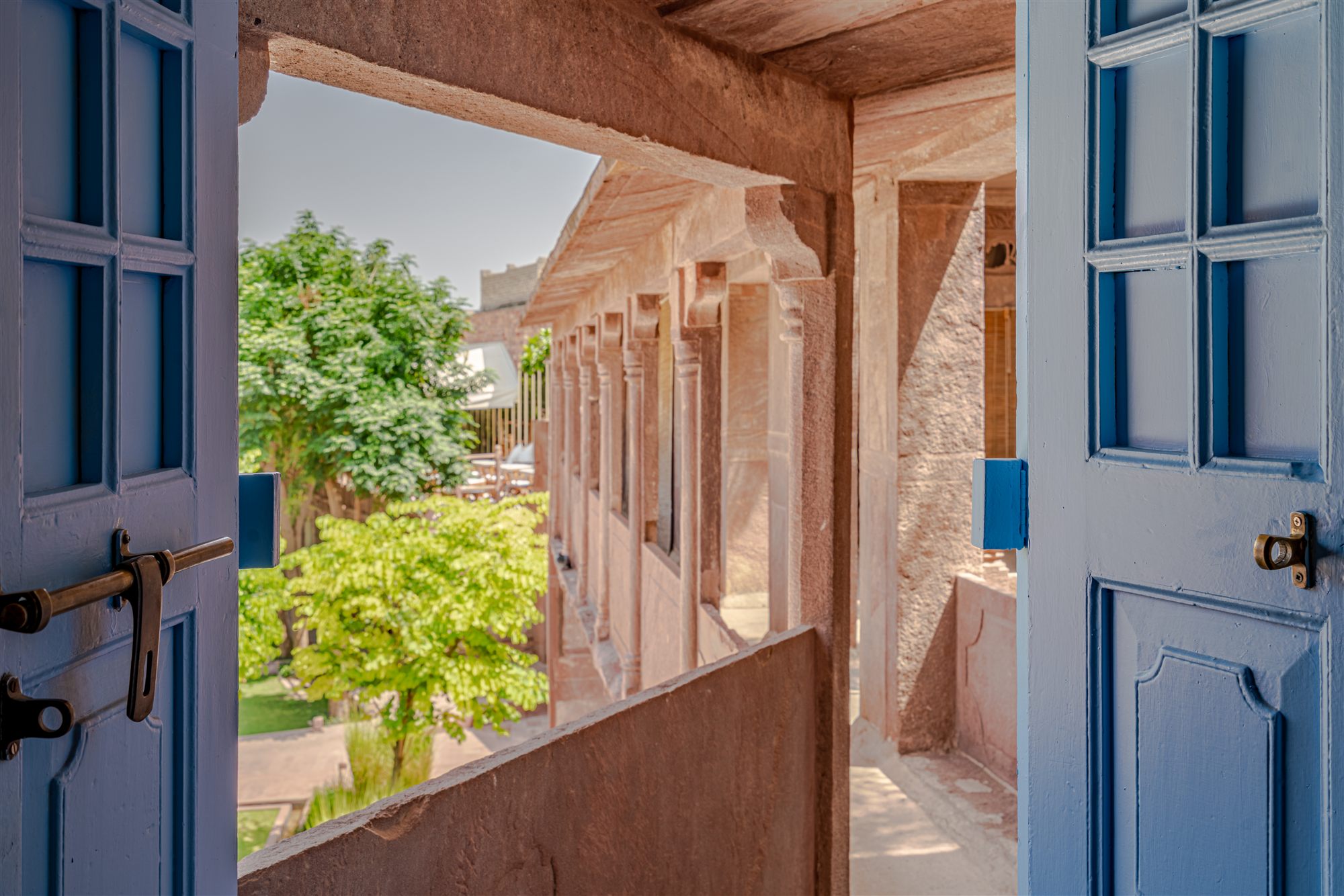 Jodhpur-blue wooden doors opening onto a sandstone veranda and garden at RAAS Jodhpur
