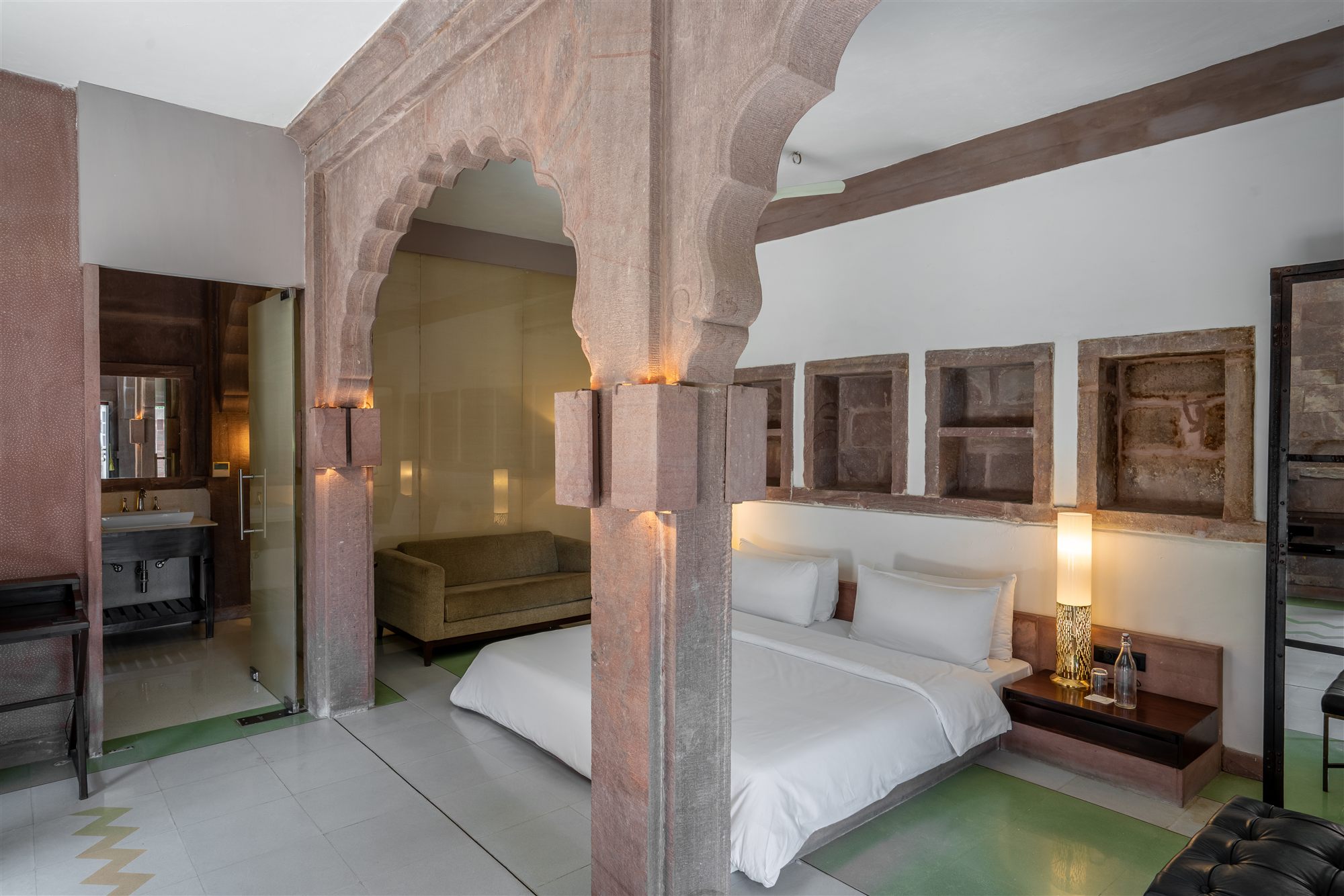 Heritage suite at RAAS Jodhpur with a carved sandstone arch, white bed and terrazzo floor