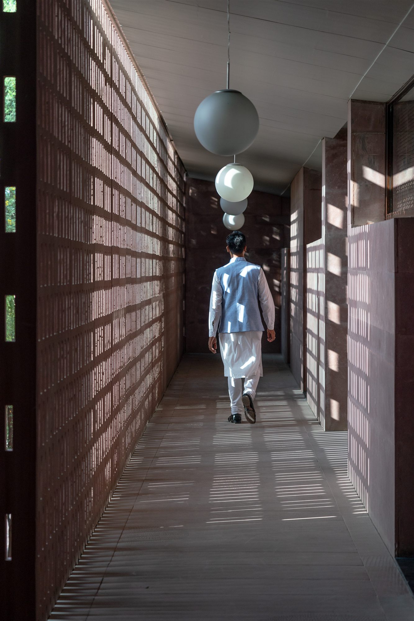 Staff member walking down a lattice-screened corridor with globe lights at RAAS Jodhpur