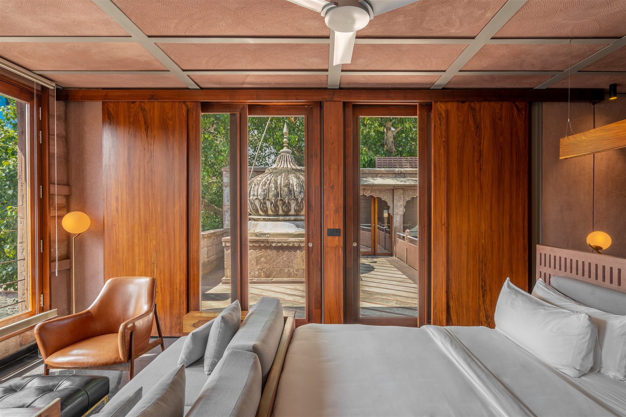 Luxury Room at RAAS Jodhpur with wood-panelled walls, leather armchair and a view of the haveli