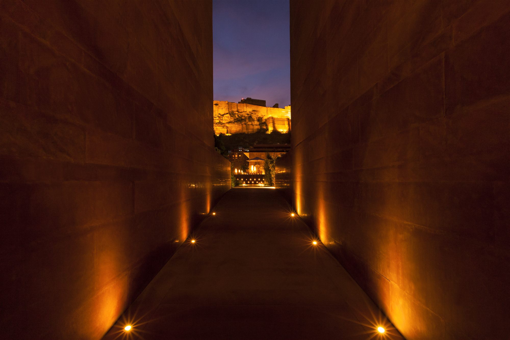 Lantern-lit sandstone passage at RAAS Jodhpur framing Mehrangarh Fort at dusk