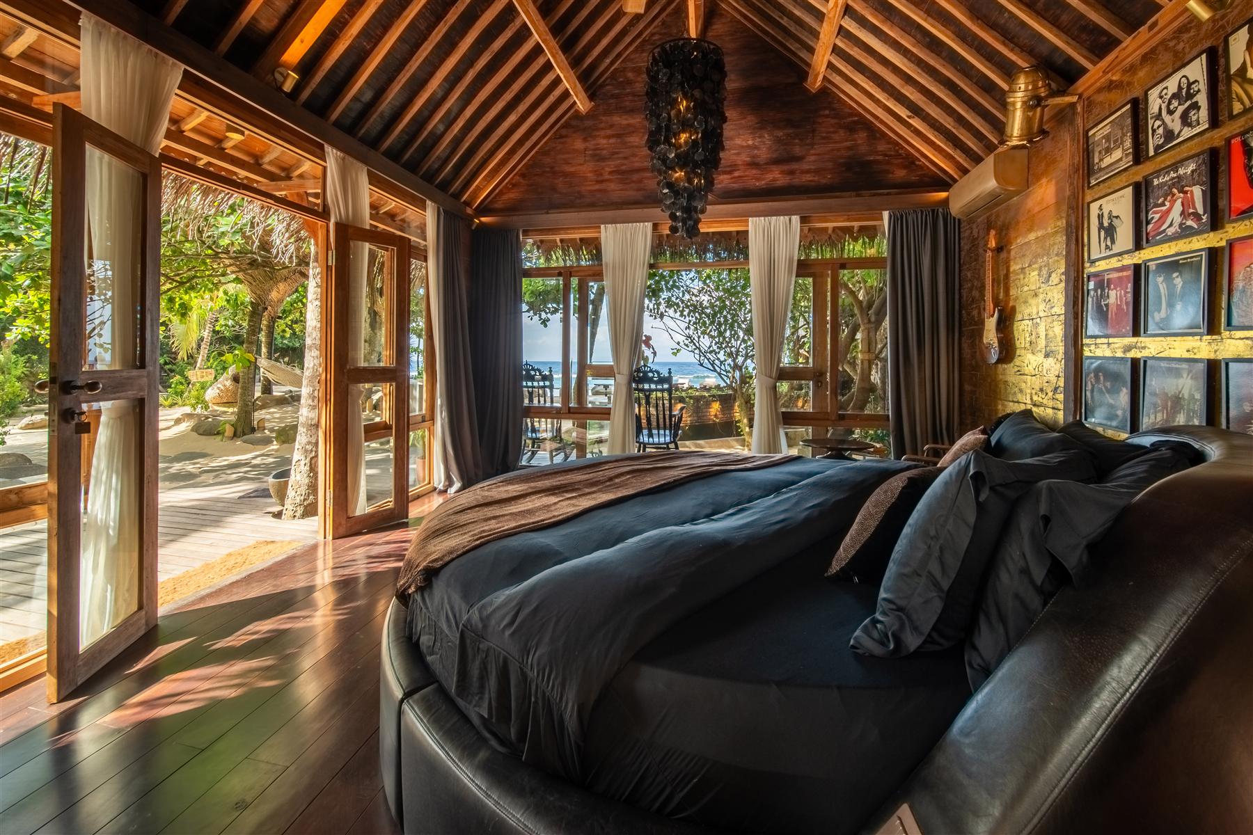 Round bed with dark linens inside a teak villa at The Seed resort, Bali, with ocean views through open doors