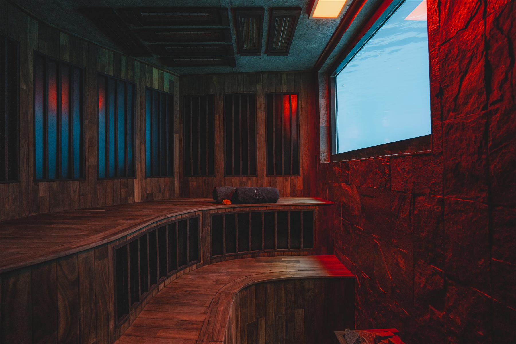 Wood-paneled sauna with curved benches and red ambient lighting at The Seed resort in Candidasa, Bali