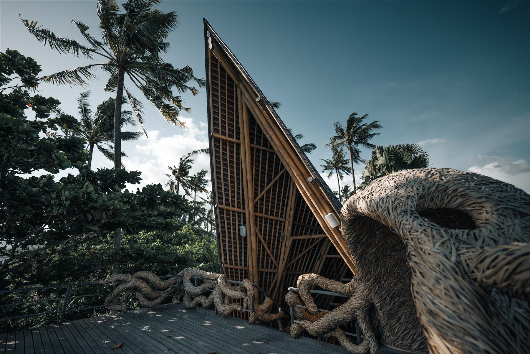 Bamboo A-frame pavilion with woven rattan sculptures on a wooden deck at The Seed resort, Candidasa, Bali