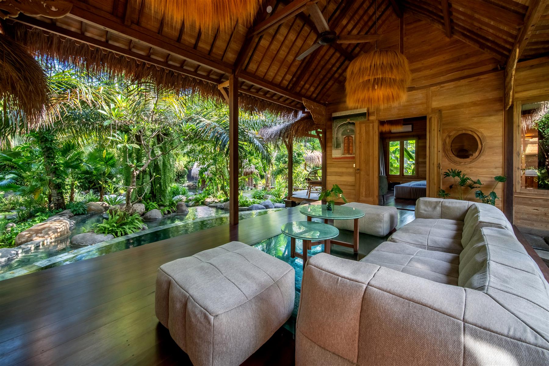 Open-air wooden lounge with beige sofas overlooking a tropical garden pond at The Seed, Bali