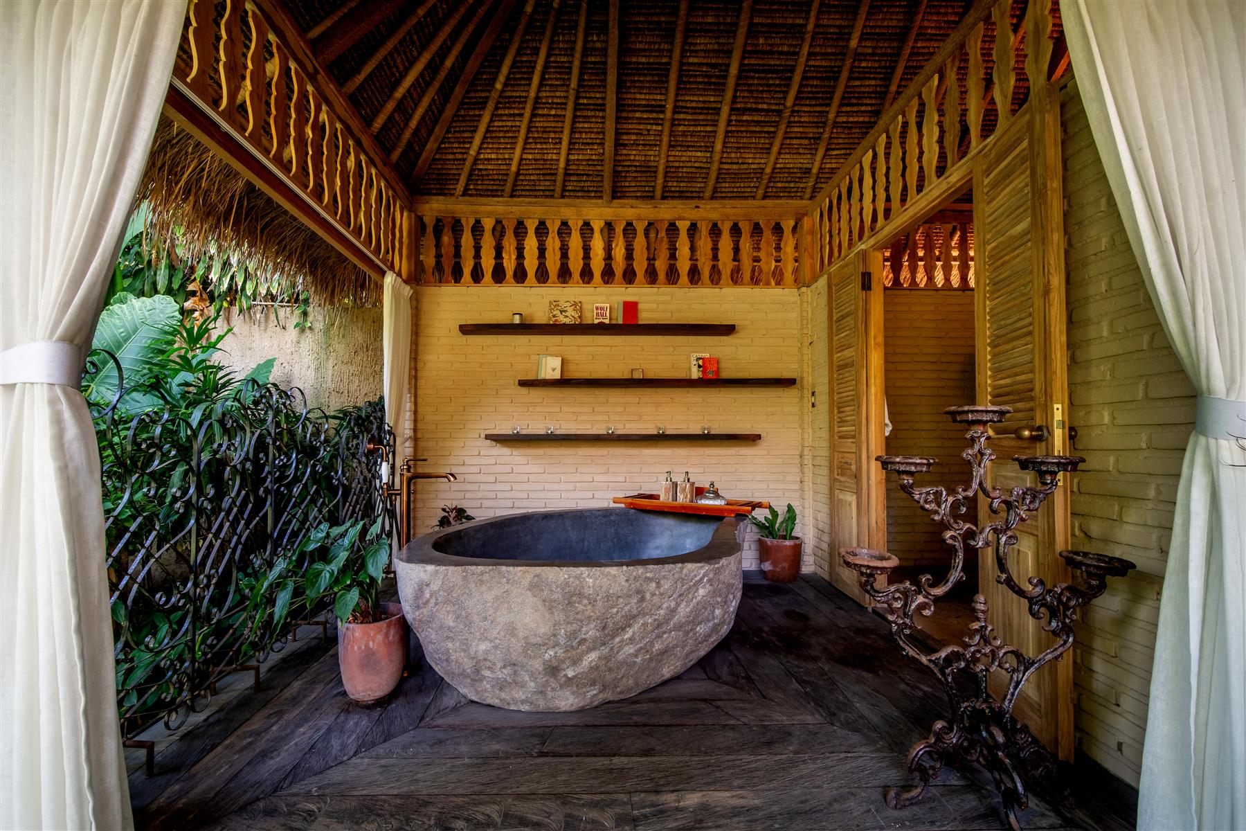 Open-air bathroom with carved stone bathtub and thatched roof at The Seed resort, Bali