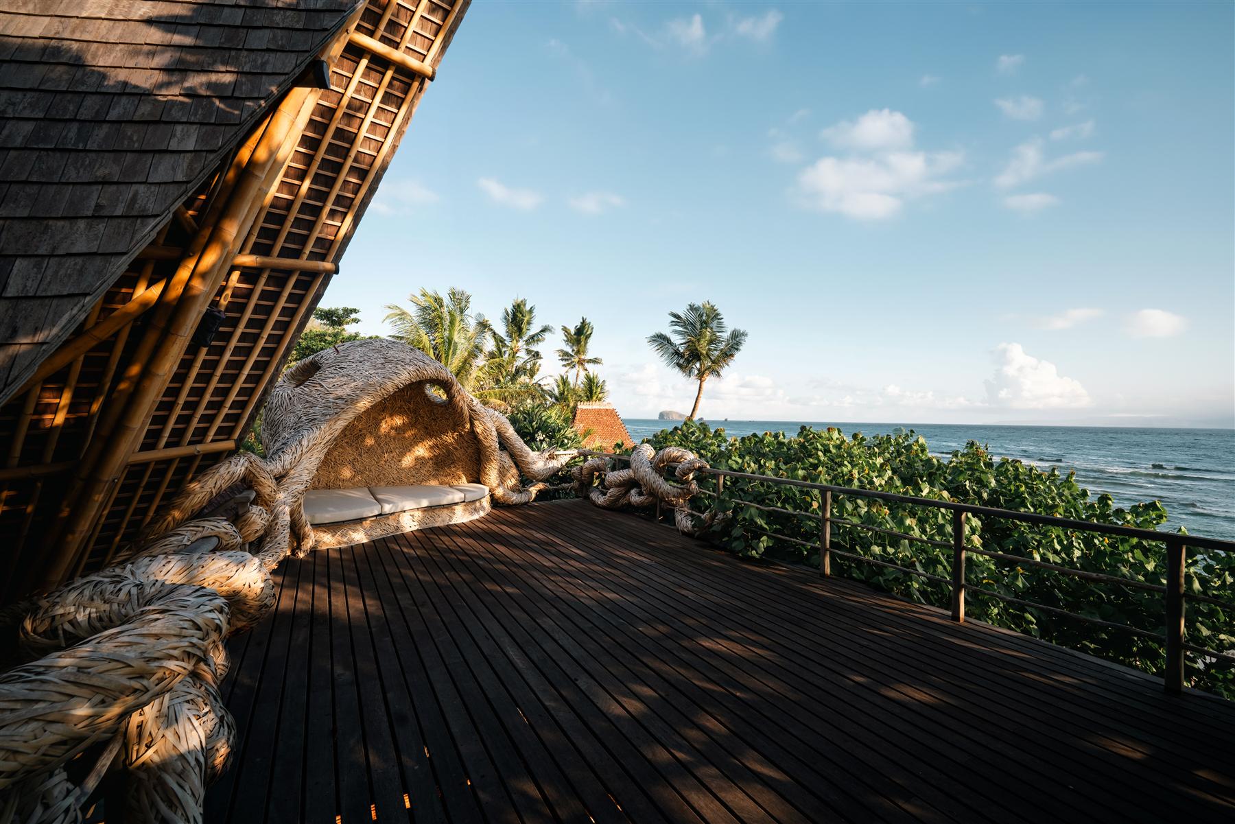 Wooden deck with woven bamboo seating at The Seed resort overlooking the ocean in Candidasa, Bali
