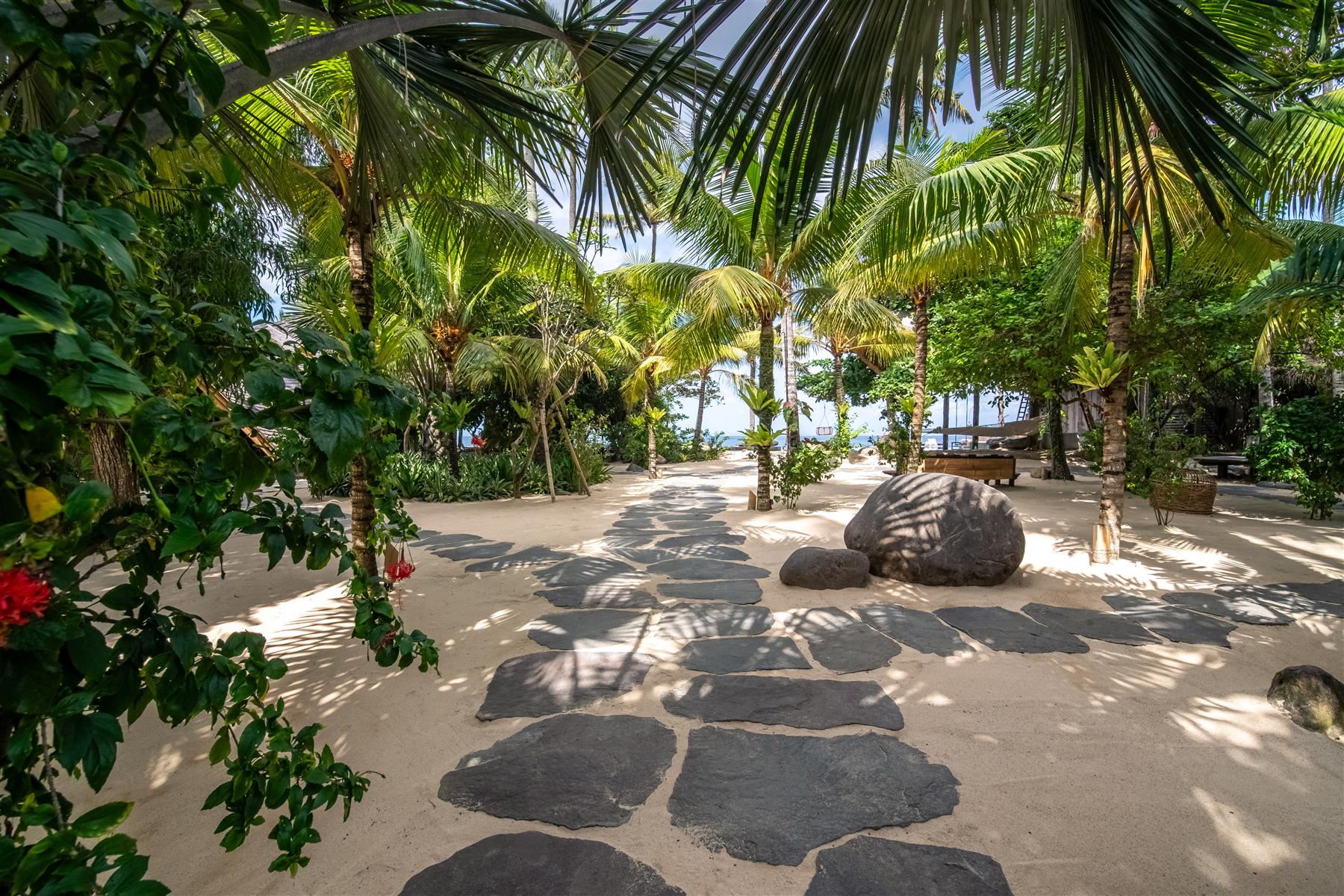 Stone pathway through tropical palm gardens leading to the ocean at The Seed resort in Candidasa, Bali