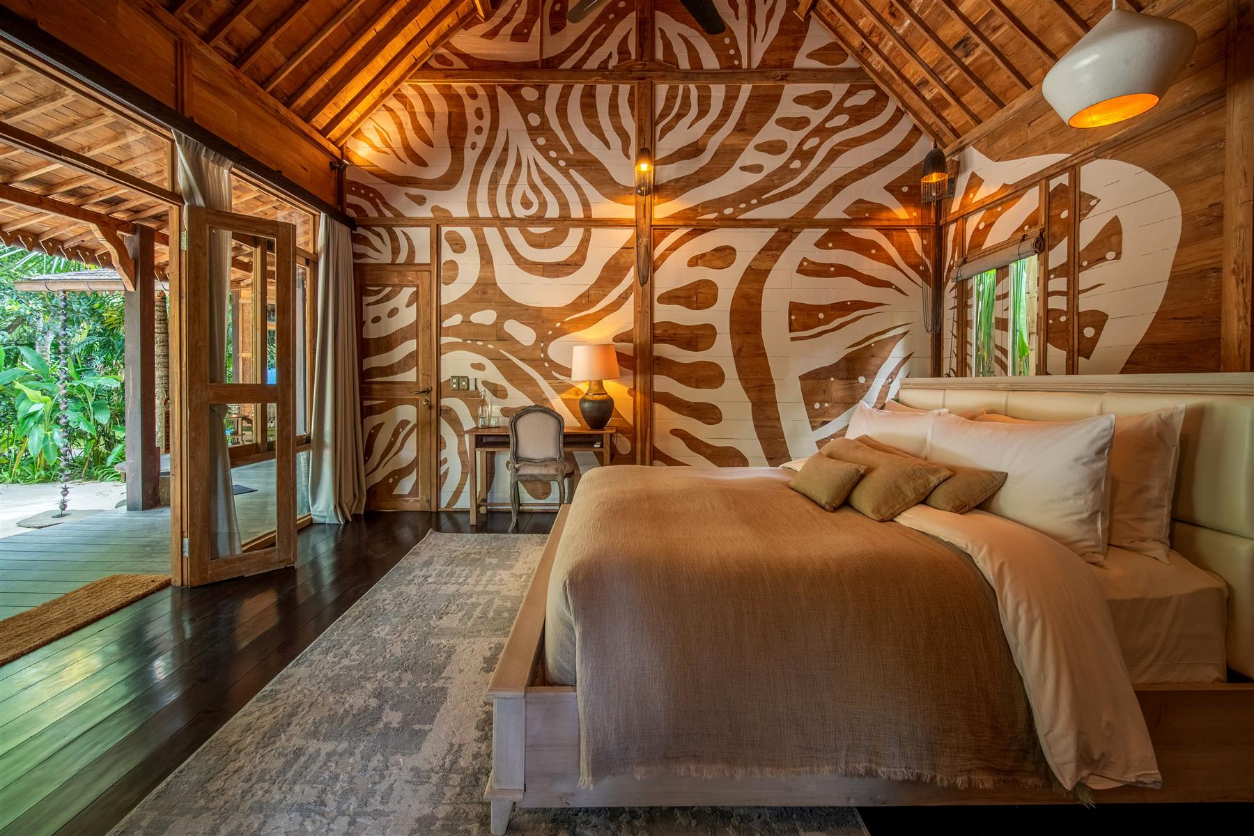 Bedroom at The Seed Bali with carved wooden mural wall, king bed, and open doors to garden terrace