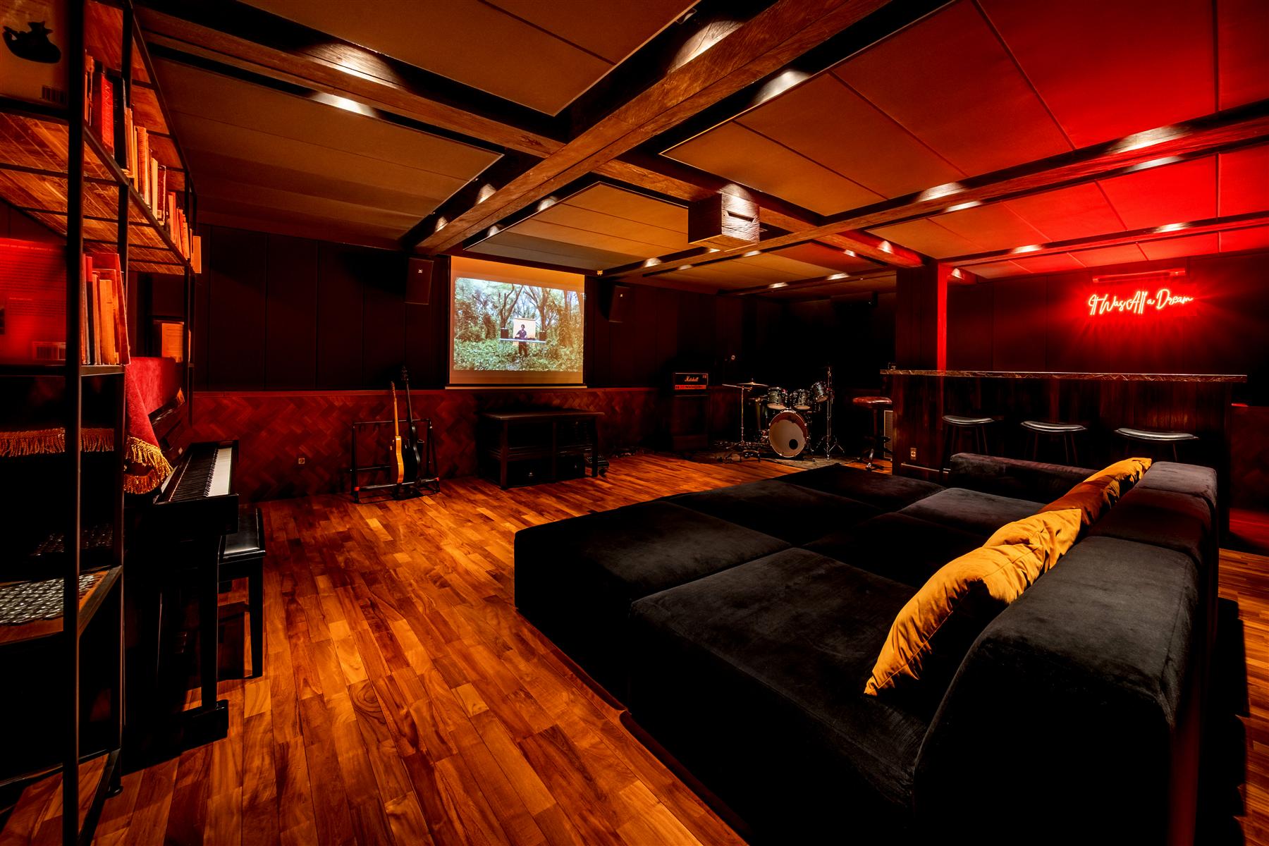 Red-lit private cinema and music lounge with black sofas, drum kit, and projector screen at The Seed, Bali