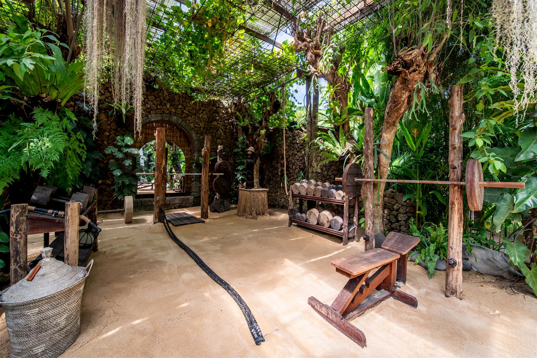 Open-air jungle gym at The Seed Bali with wooden weights, stone walls, and hanging tropical plants