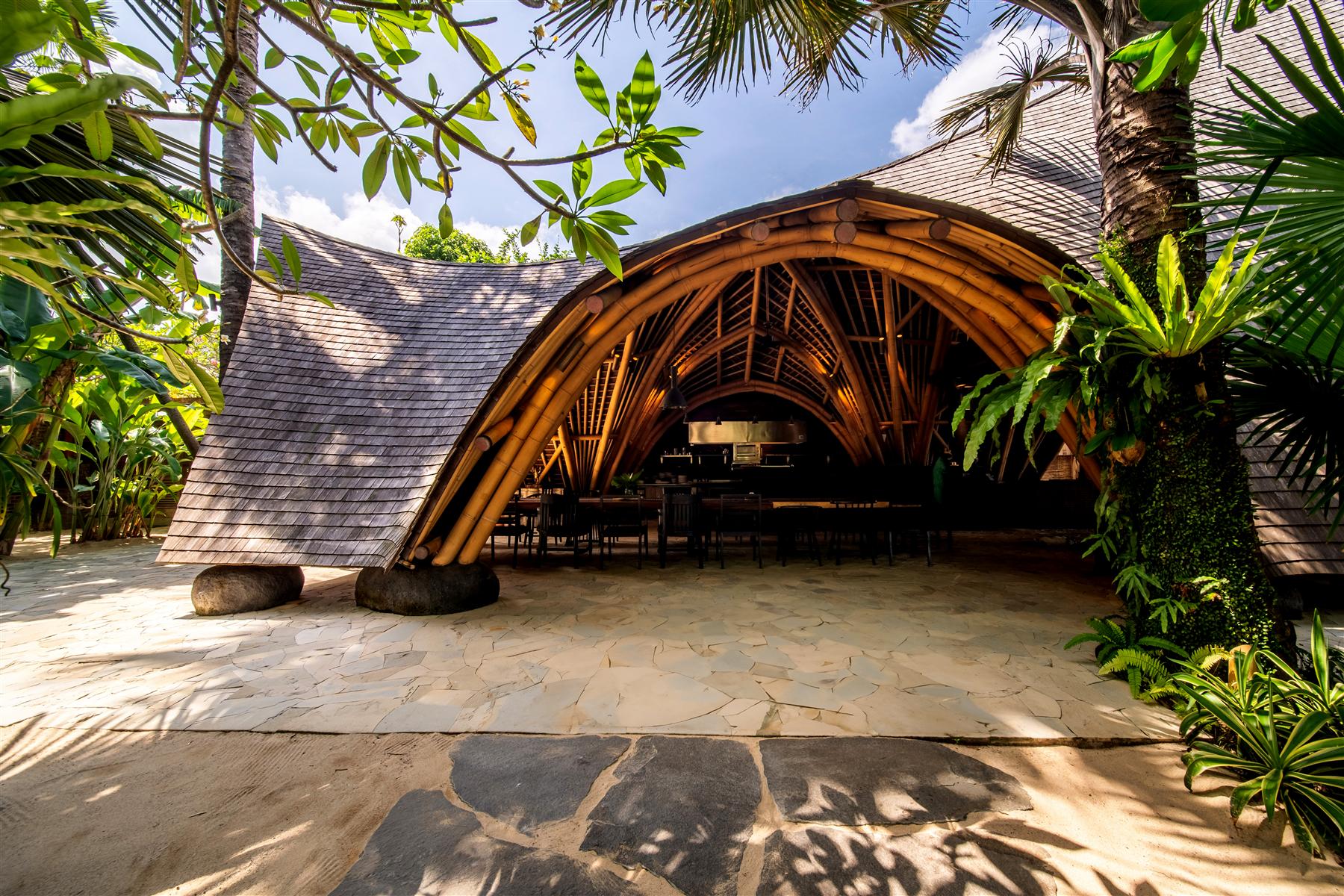Bloom Kitchen's curved bamboo arch and shingled roof among tropical palms at The Seed, Bali