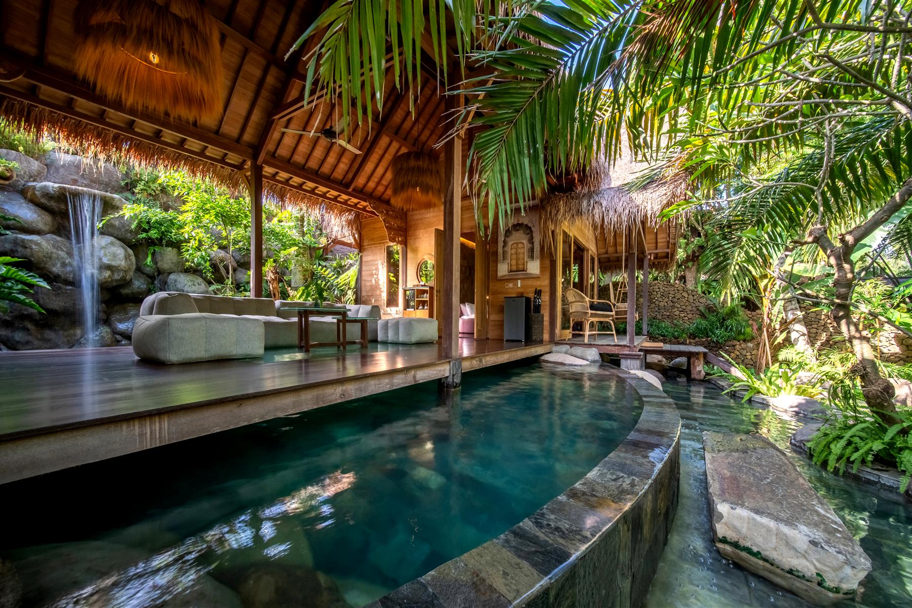 Private villa pool deck with thatched roof, waterfall, and tropical gardens at The Seed, Bali