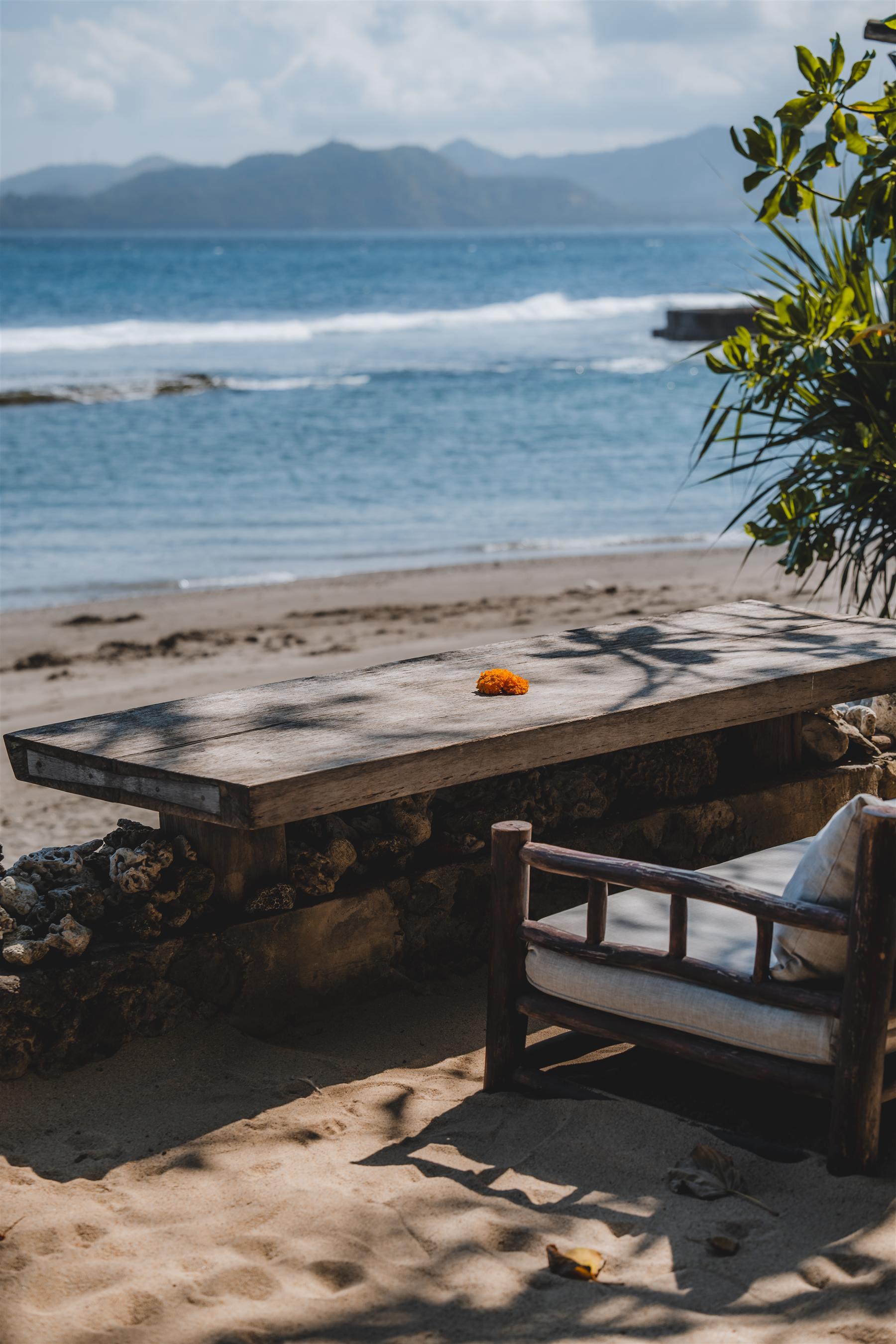 Beachfront wooden table and chair on the sand at The Seed resort in Candidasa, Bali, overlooking the ocean