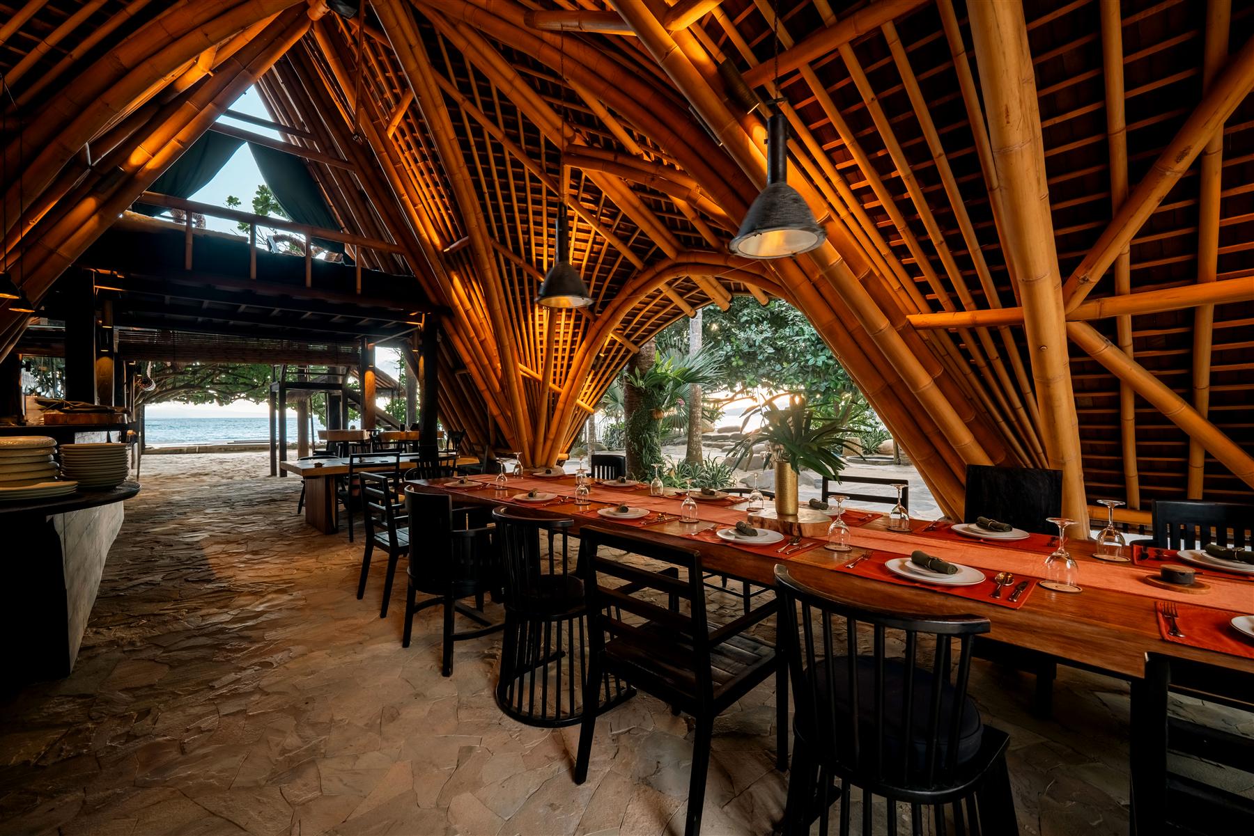 Bamboo-vaulted dining pavilion at The Seed resort in Candidasa, Bali, with set tables overlooking the ocean
