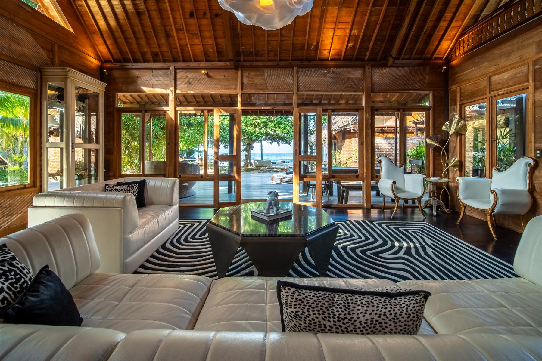 The Seed Bali resort lounge with white leather sofas, wood-paneled walls, and ocean views through open doors