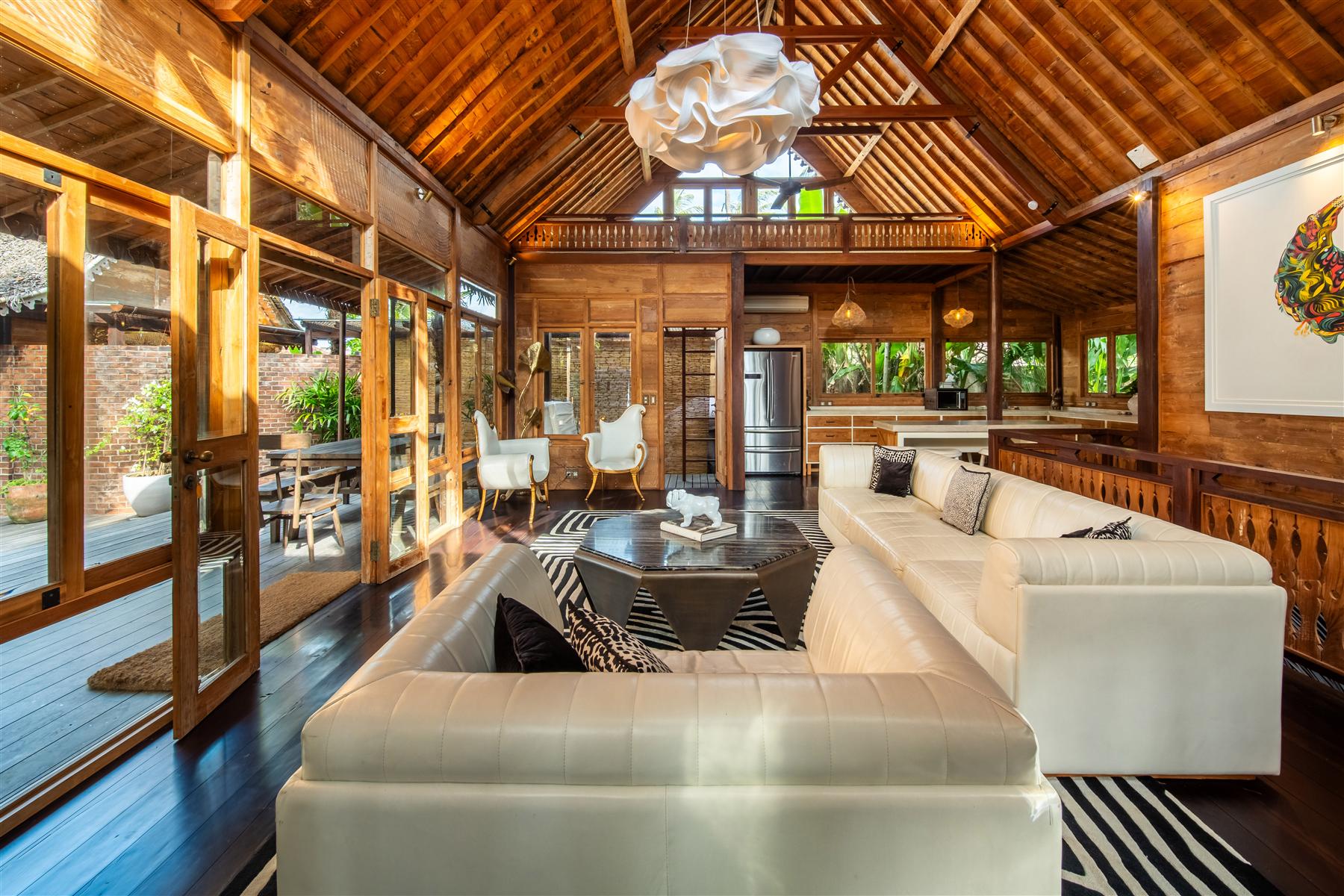 Open-air living room at The Seed Bali with white leather sofas, vaulted timber ceiling, and garden views